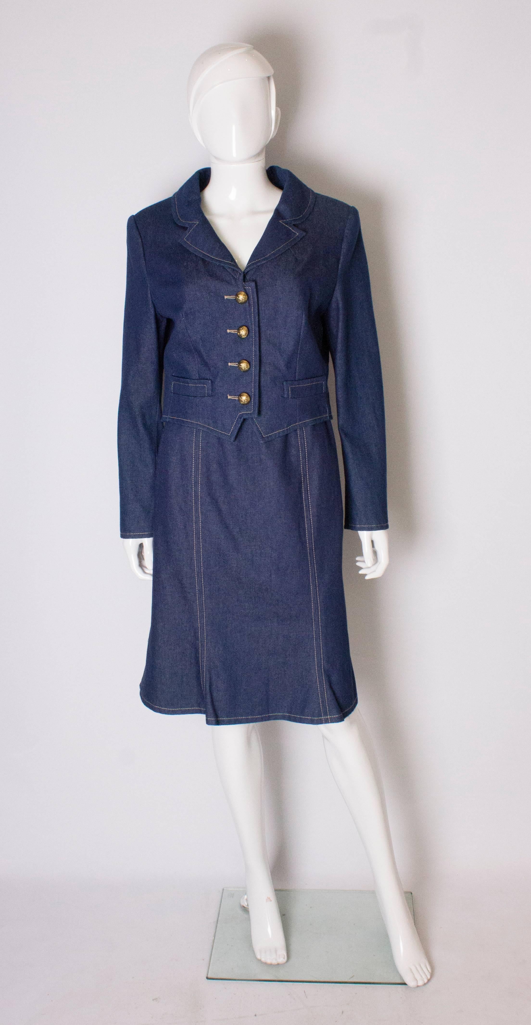 Un tailleur jupe chic du designer britannique Donald Campbell.  Dans un tissu denim bleu, la veste a un col en V avec une ouverture à 4 boutons, et 3 boutons sur chaque poignet, et est entièrement doublée. La jupe a une fermeture éclair centrale au