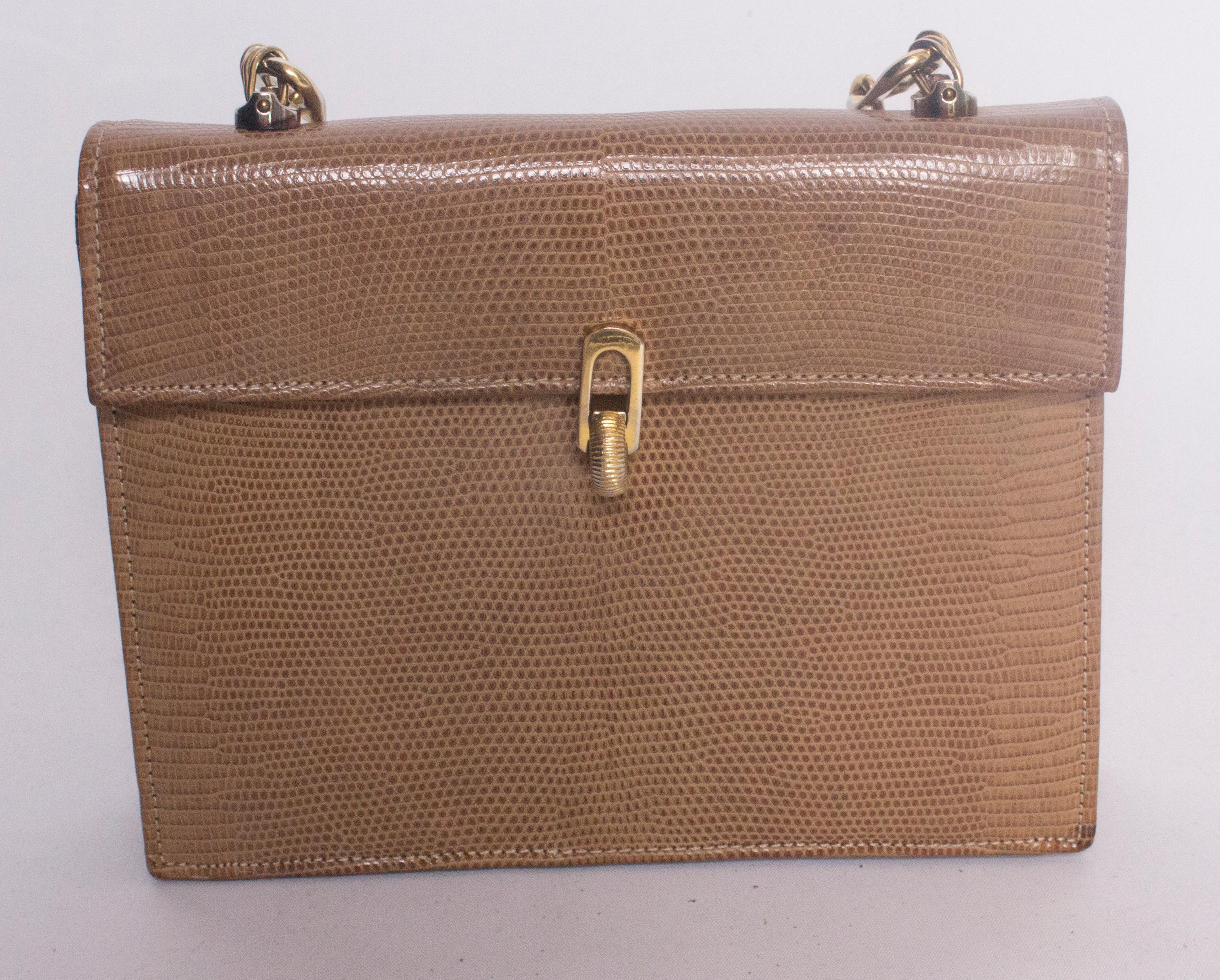 A chic vintage lizzard skin handbag with a nice heavy gold chain. The bag is biscuit coloured lizard and leather lined. It has a foldover flap with decorative catch. Internally there are two compartments, one has one zip pocket and one pouch pocket,