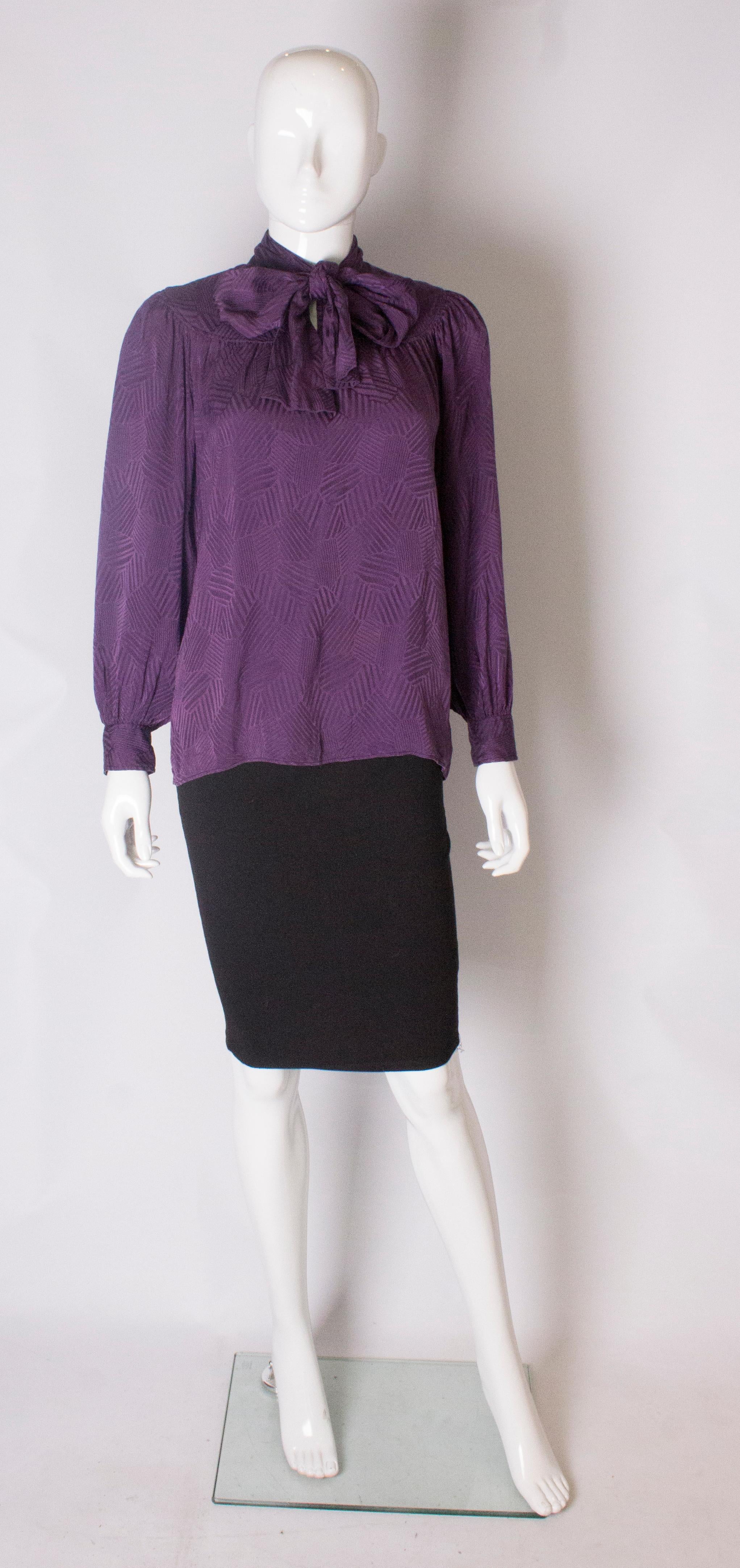 A chic blouse by Yves Saint Laurent ,Rive Gauche.The blouse is in a purple textured silk. It has a yoke front and back,  with a two button opening at the neck and single button cuffs, and a puusy bow tie.