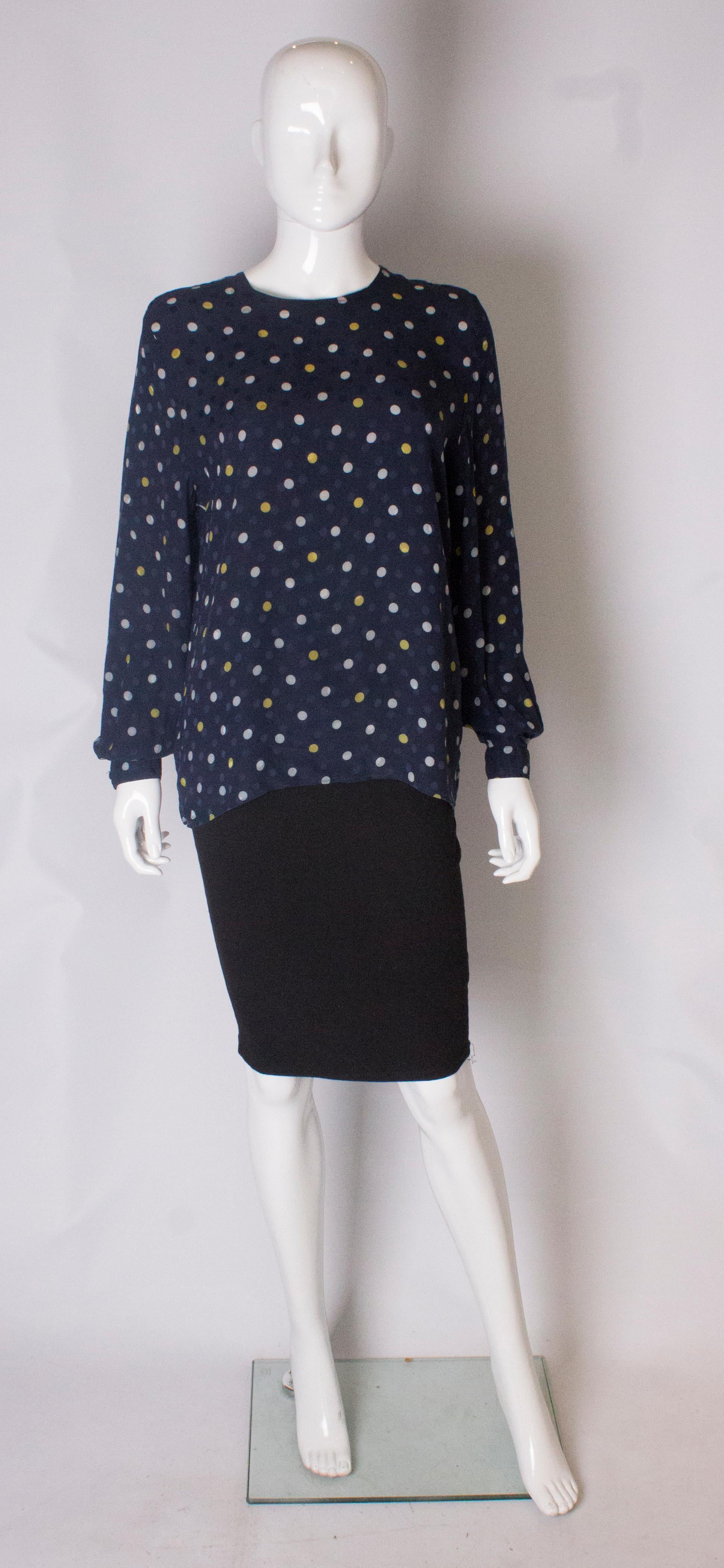  A chic silk blouse by Valentino. The blouse has long sleeves with a single button cuff, and a button opening at the back. The silk has blue dots in the background with yellow and white spots in the foreground.
