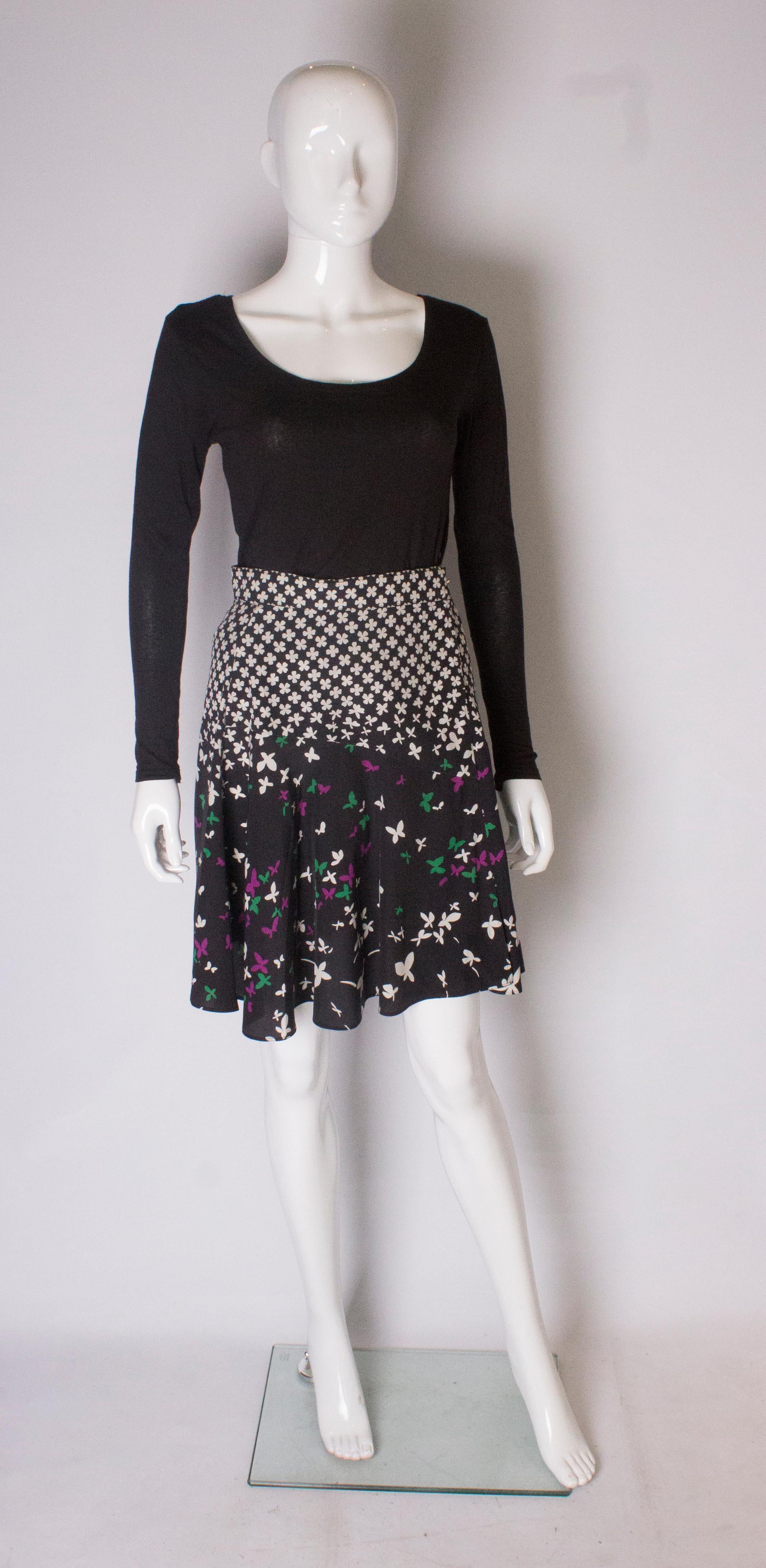 A chic silk wrap over skirt by Yves Saint Laurent. The skirt is made of silk with a black background and ivory print  on the top half. The lower area has a black background with an ivory, green and plum colour print.