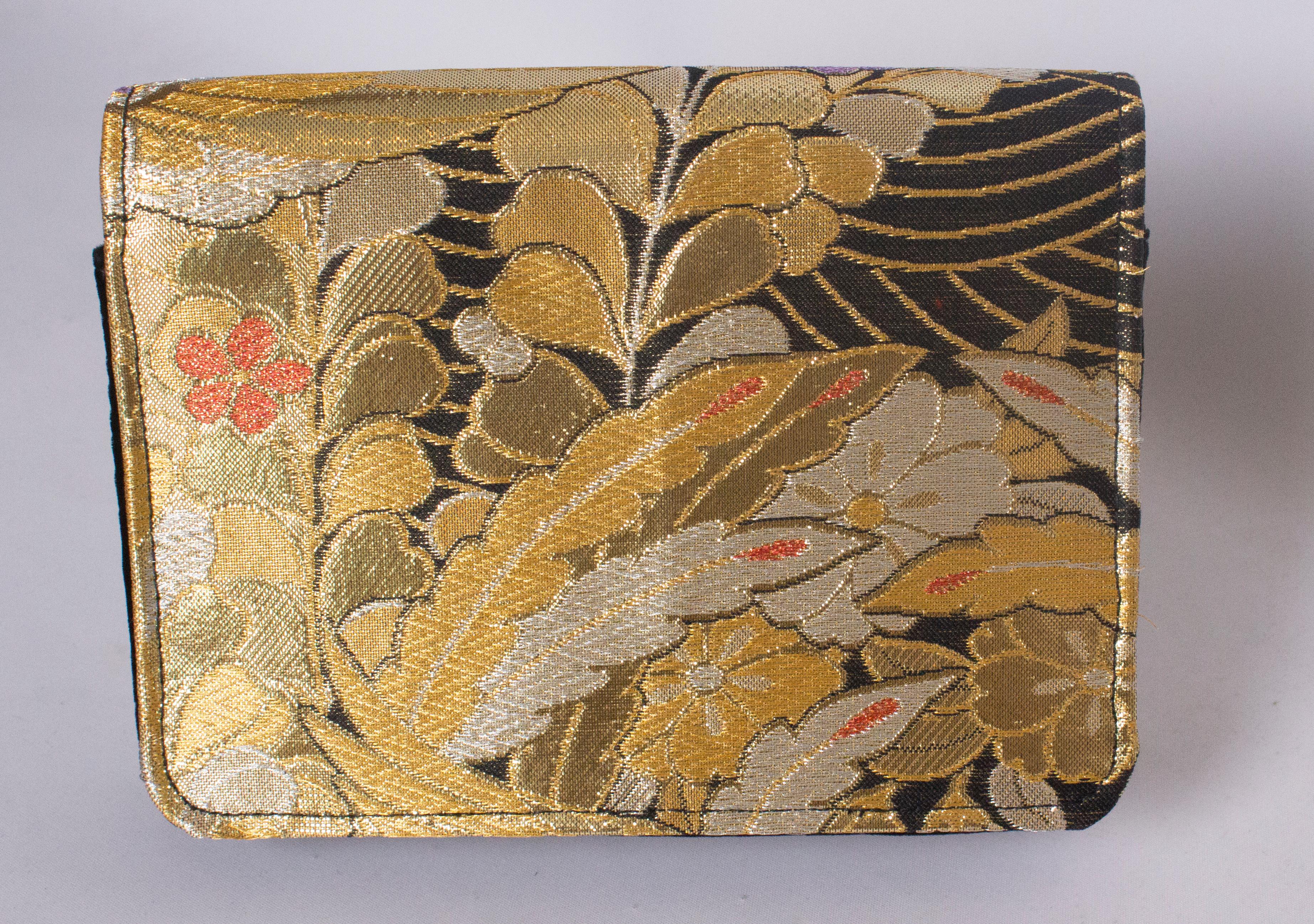 A chic bag by Mame Huku. The bag is made from vintage japanease silk textiles. This one is covered front and back in a gold , black, silver, red and lilac design. It has a fold over flap opening, and has a magnetic fastening. The bag is lined in