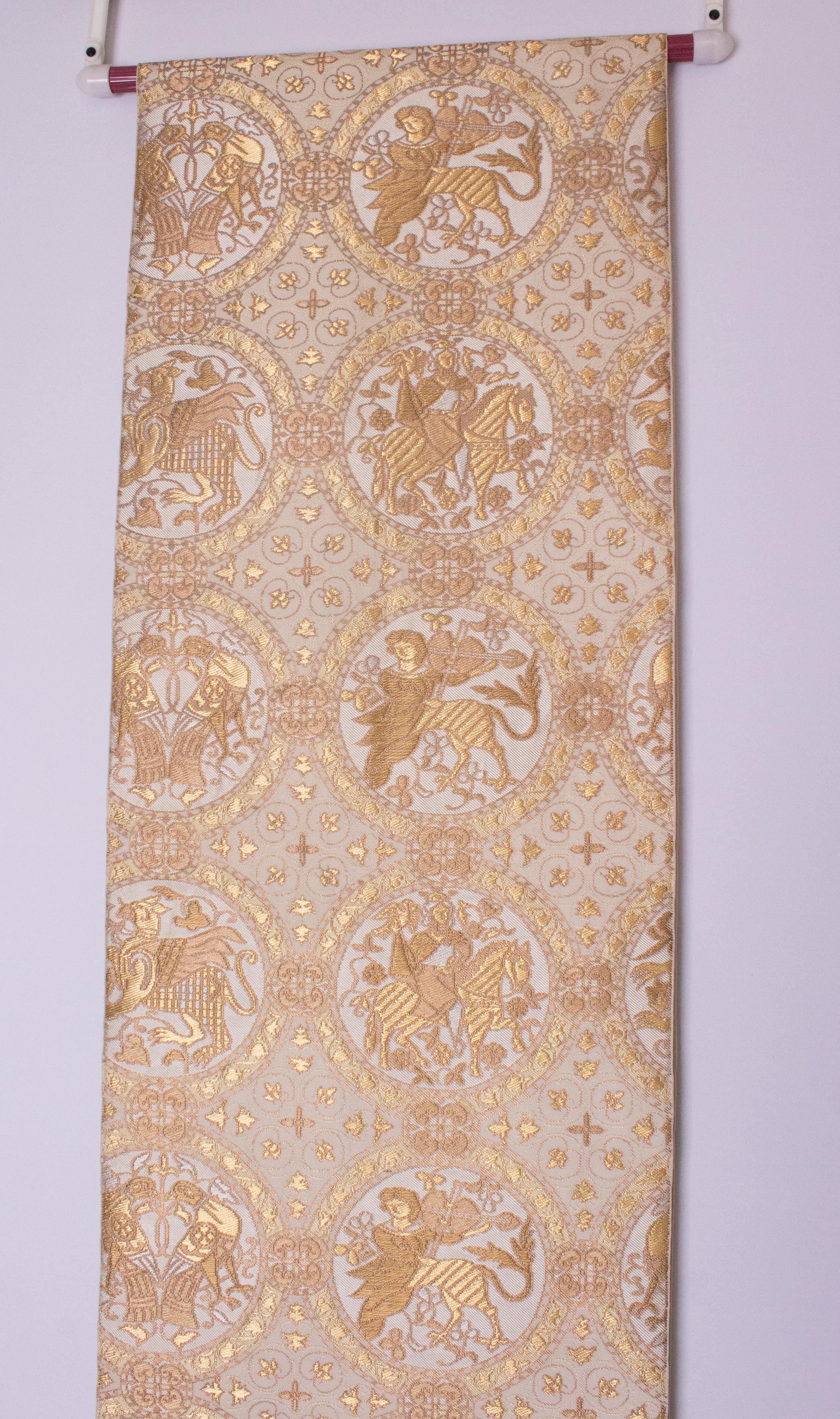 A chic silk obi belt in a gold heraldic design. The belt has an ivory background, with a gold heraldic print. The belt measures 173'' long and 12 1/2 in height. The embroidered parts are 110'' and 18 1/2'' long.