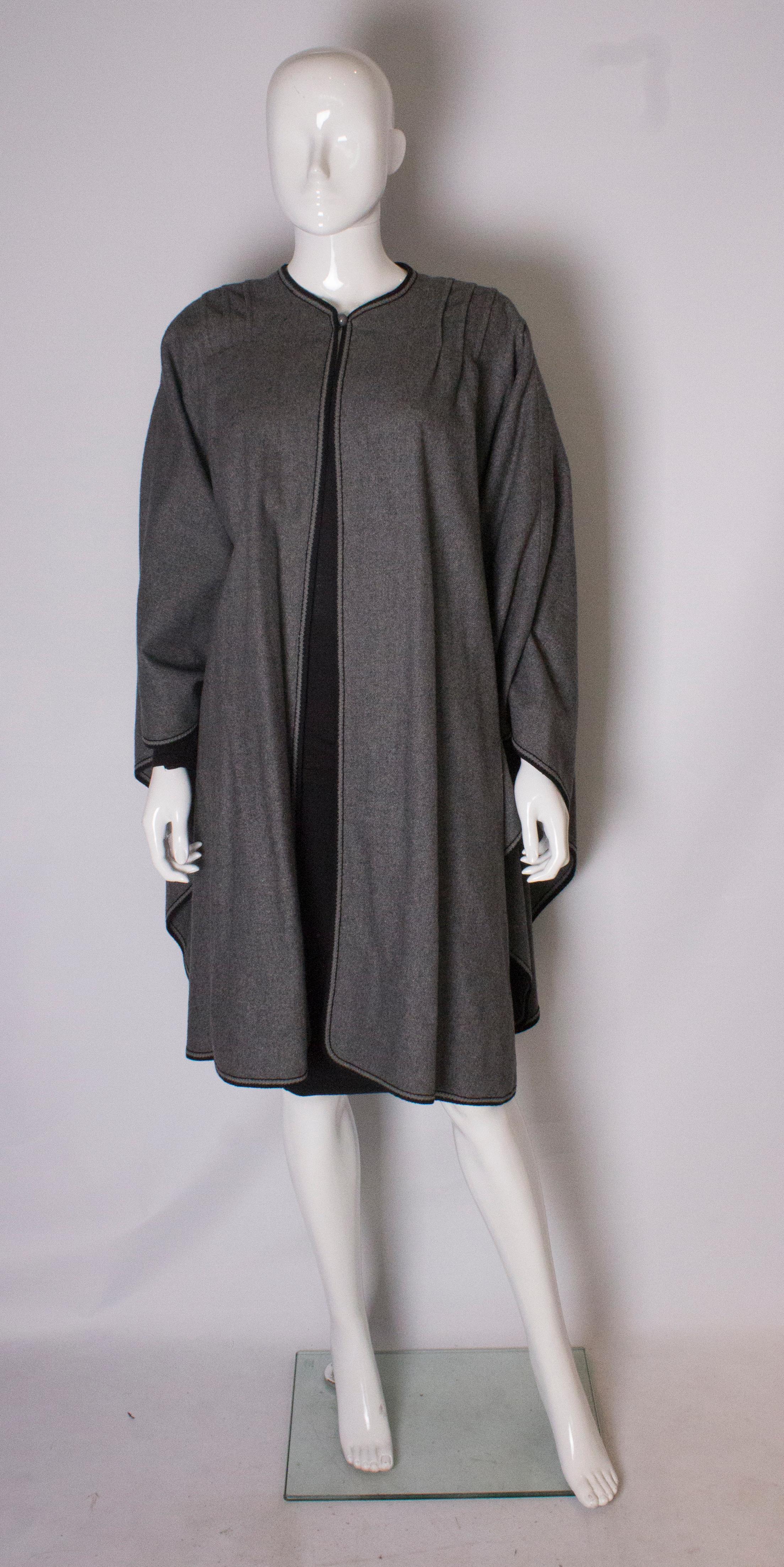 A chic cape, ideal for Fall. In grey wool, the cape has pintucks on the shoulders and a one button fastening at the neck.  It is loose fitting ,and can fit a bust up to 42'', length 40''.