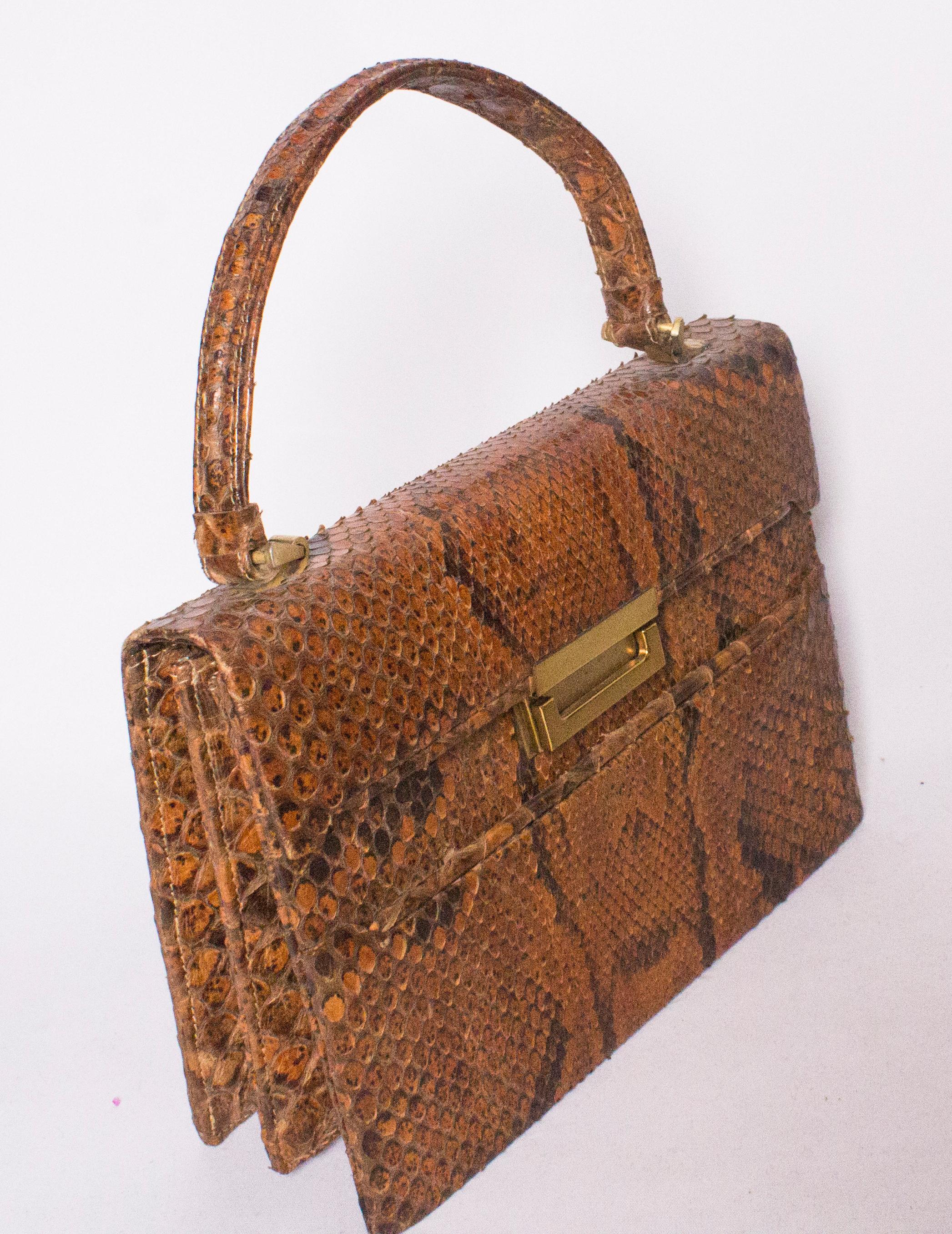 A chic tophandle snakeskin bag in tan and dark brown. The bag has a flap front with clasp.  There is a pouch pocket at the front, and internally there are two compartments each with a pouch pocket.
Height 7'', width 9'', depth 2 1/2''