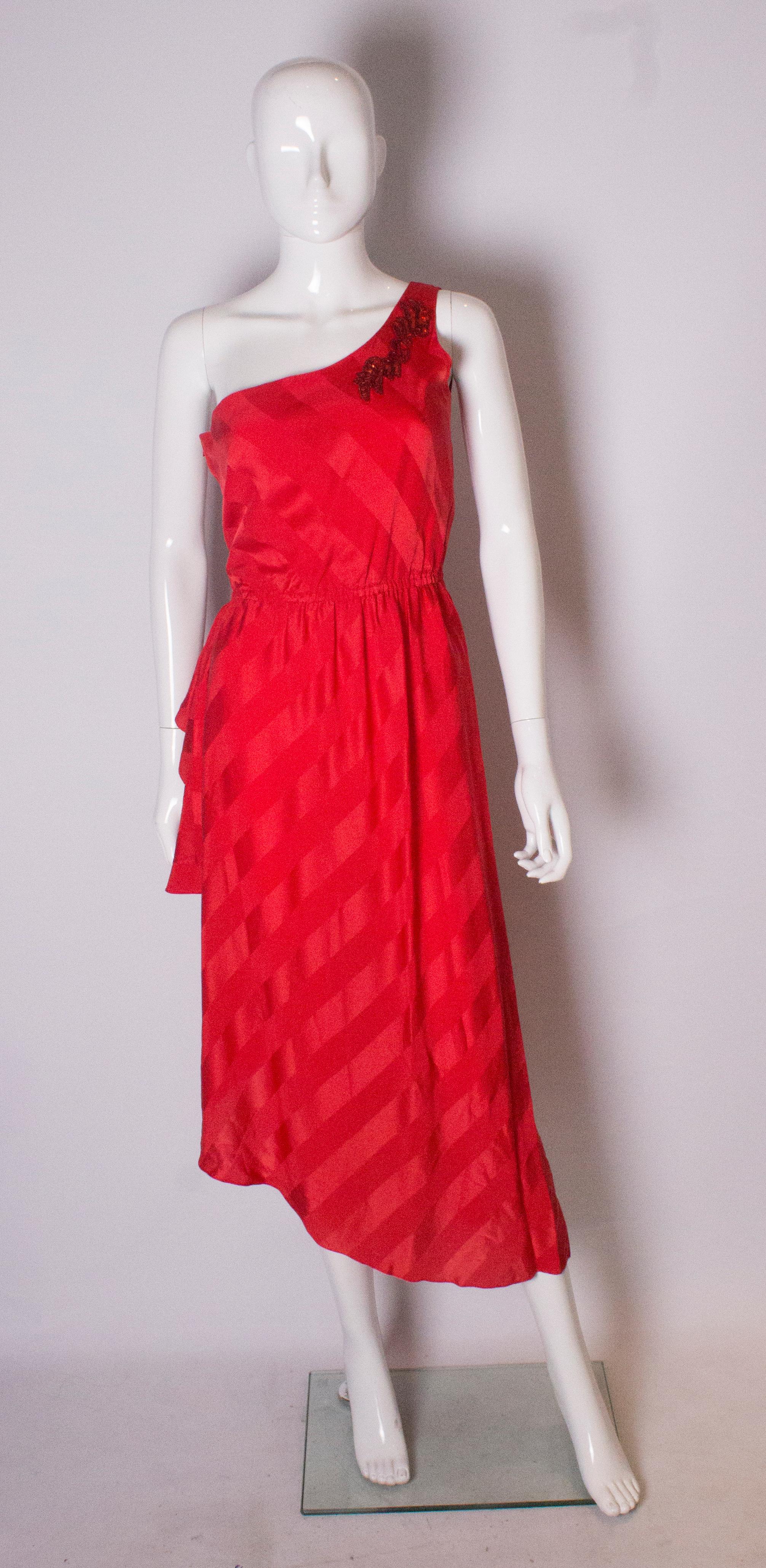 A great party dress by Bruce Oldfield . In a red silk, with a self stripe effect, the dress has one shoulder and an asymetric skirt . There is embellishment on the shoulder, a lined bodice, and a side zip opening, with an elastic waist.