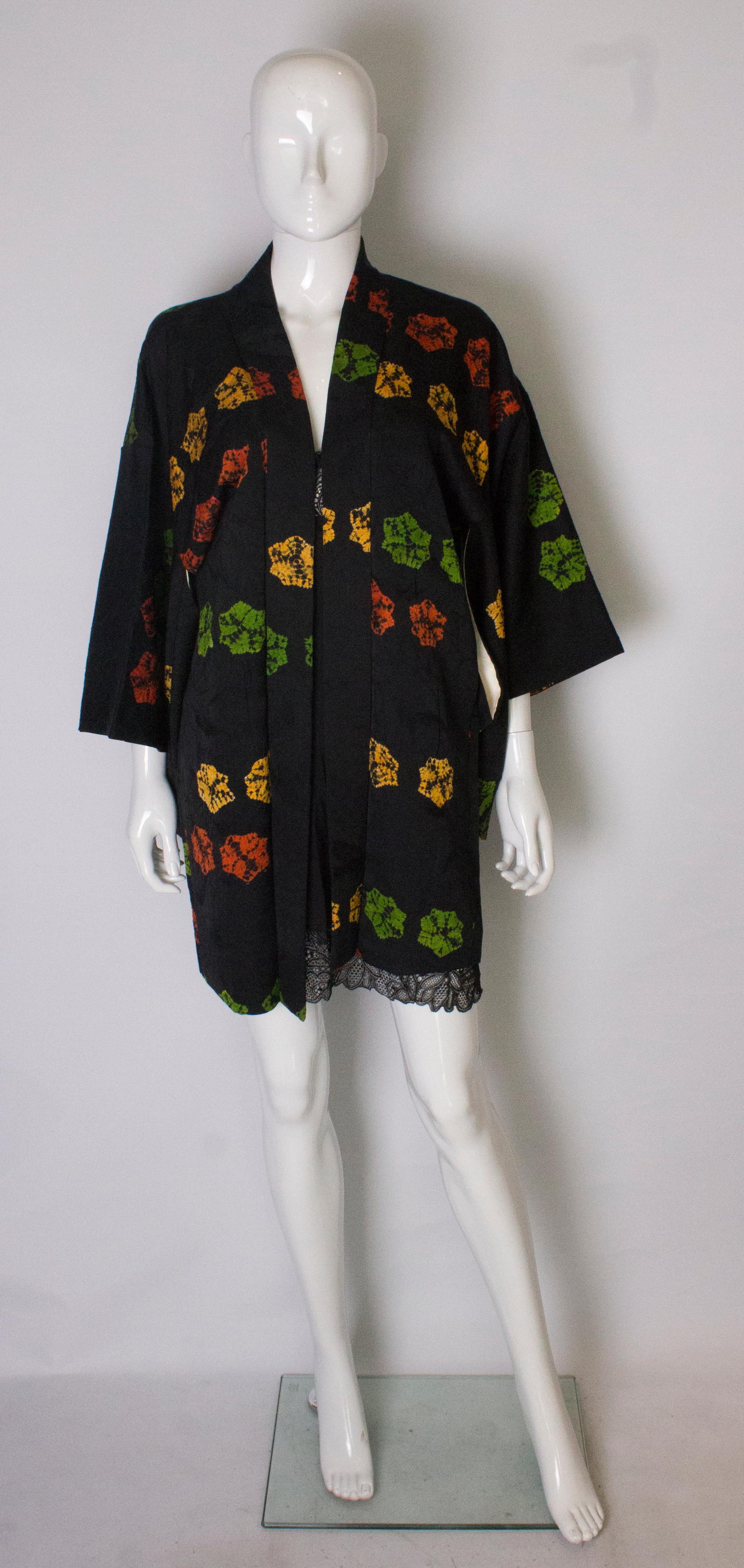 A chic short black kimono with floral decoration. The black textured fabric is decorated with flowers in various colours and the kimono has a yellow and pink floral lining.