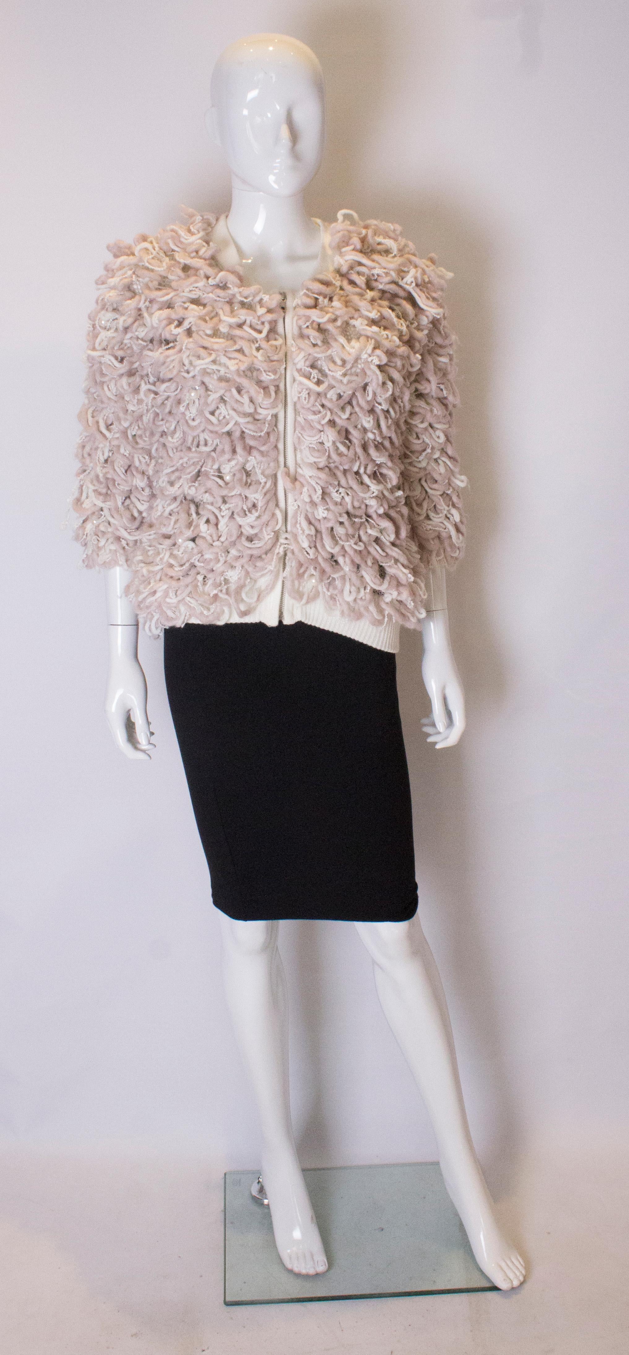 A warm and unusual jacket. The jacket is in a soft pink and white with ribbing at the hem and collar.  It has a v nekcline with a zip front opening and is decorated with pearls and diamante.