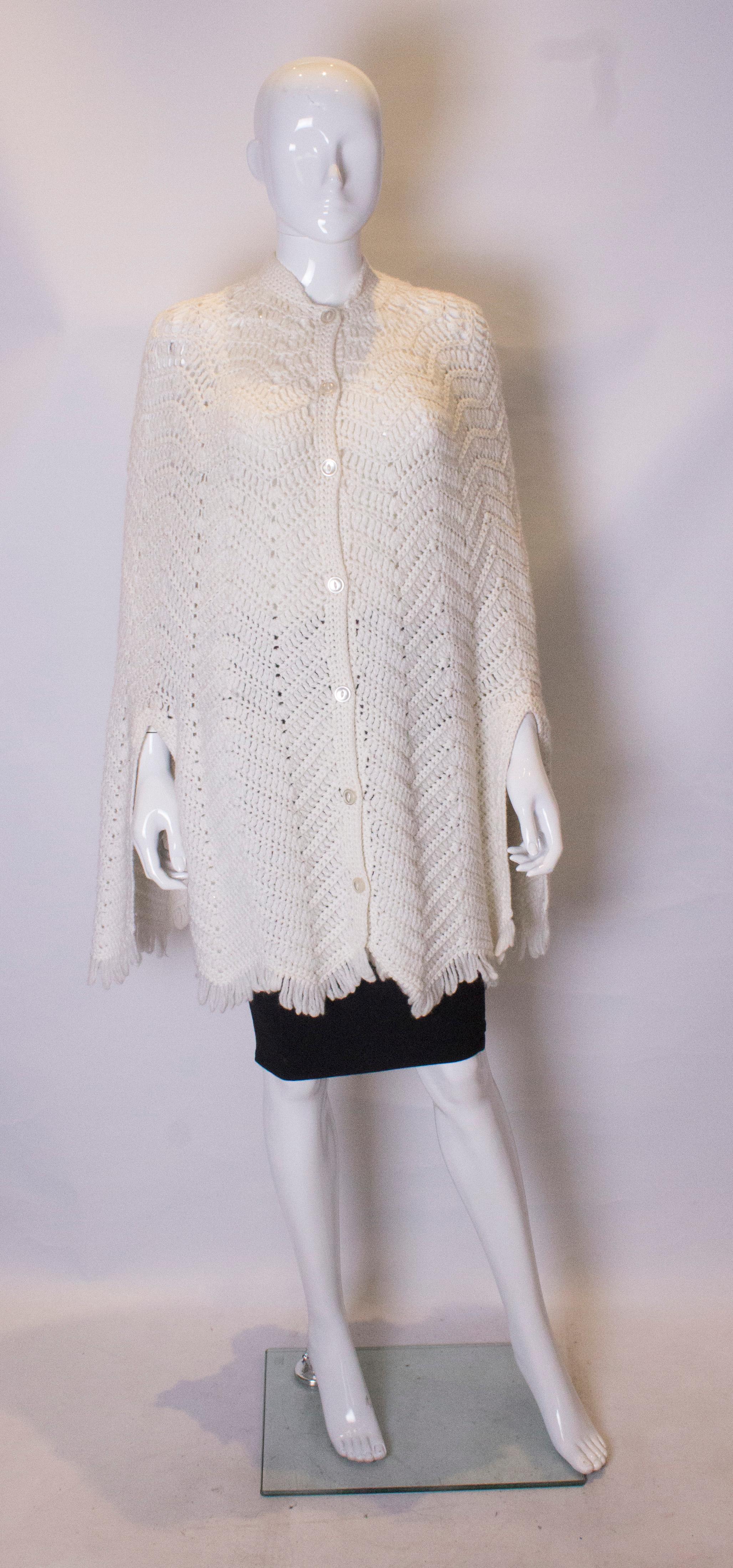 A chic vintage hand knitted cape. The cape has a round neckline with central button opening. It has a scalloped hem with fringing and two 11'' slits for arms etc. Measurements : shoulder to shoulder 19'', length 34''