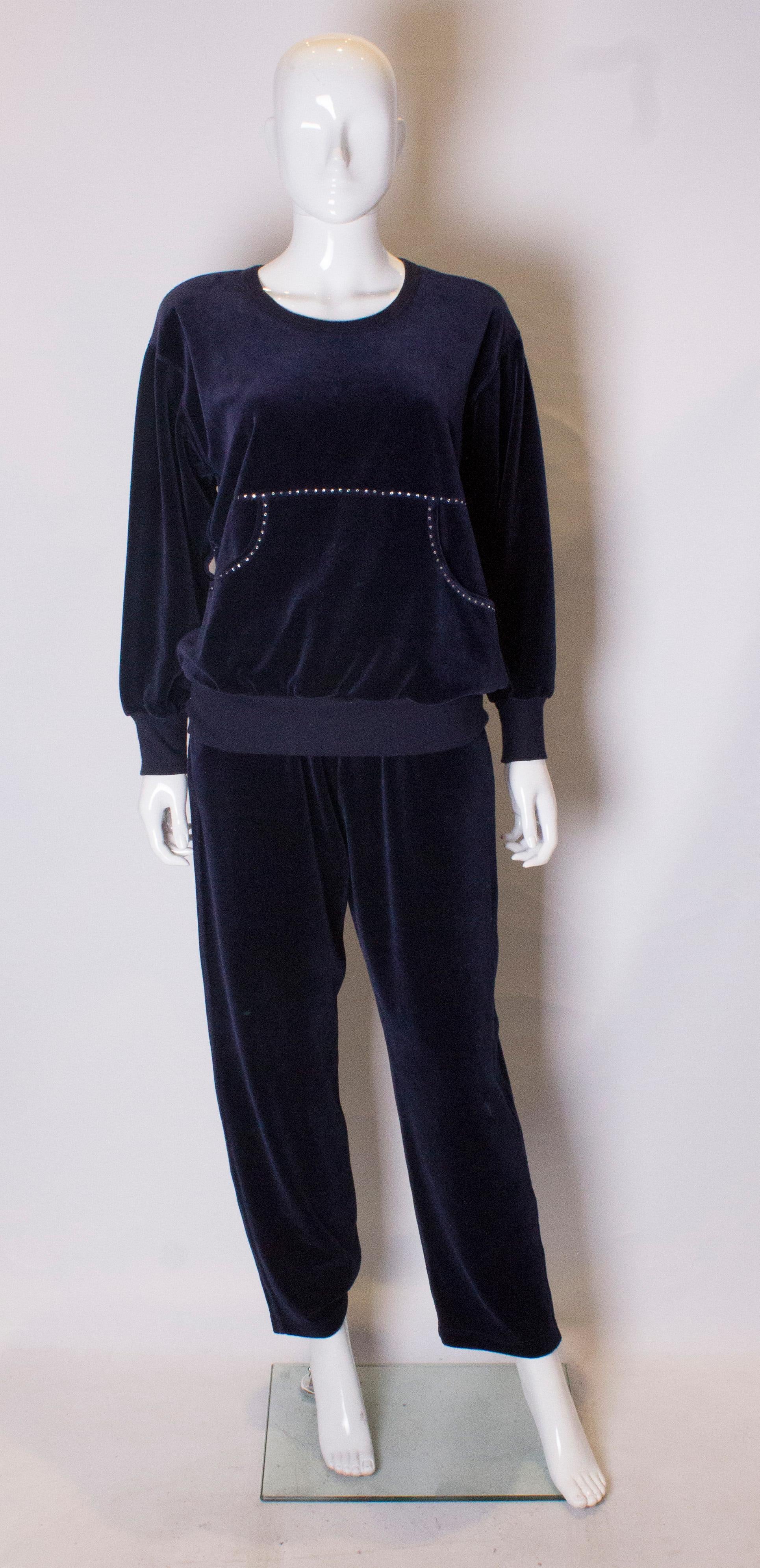 Un abito per il tempo libero super elegante di Sonia Rykiel. Il vestito è in velluto blu intenso, con due tasche a marsupio sul davanti. Il top ha uno scollo rotondo e un dettaglio di diamanti sul davanti e sul retro. I pantaloni hanno una vita