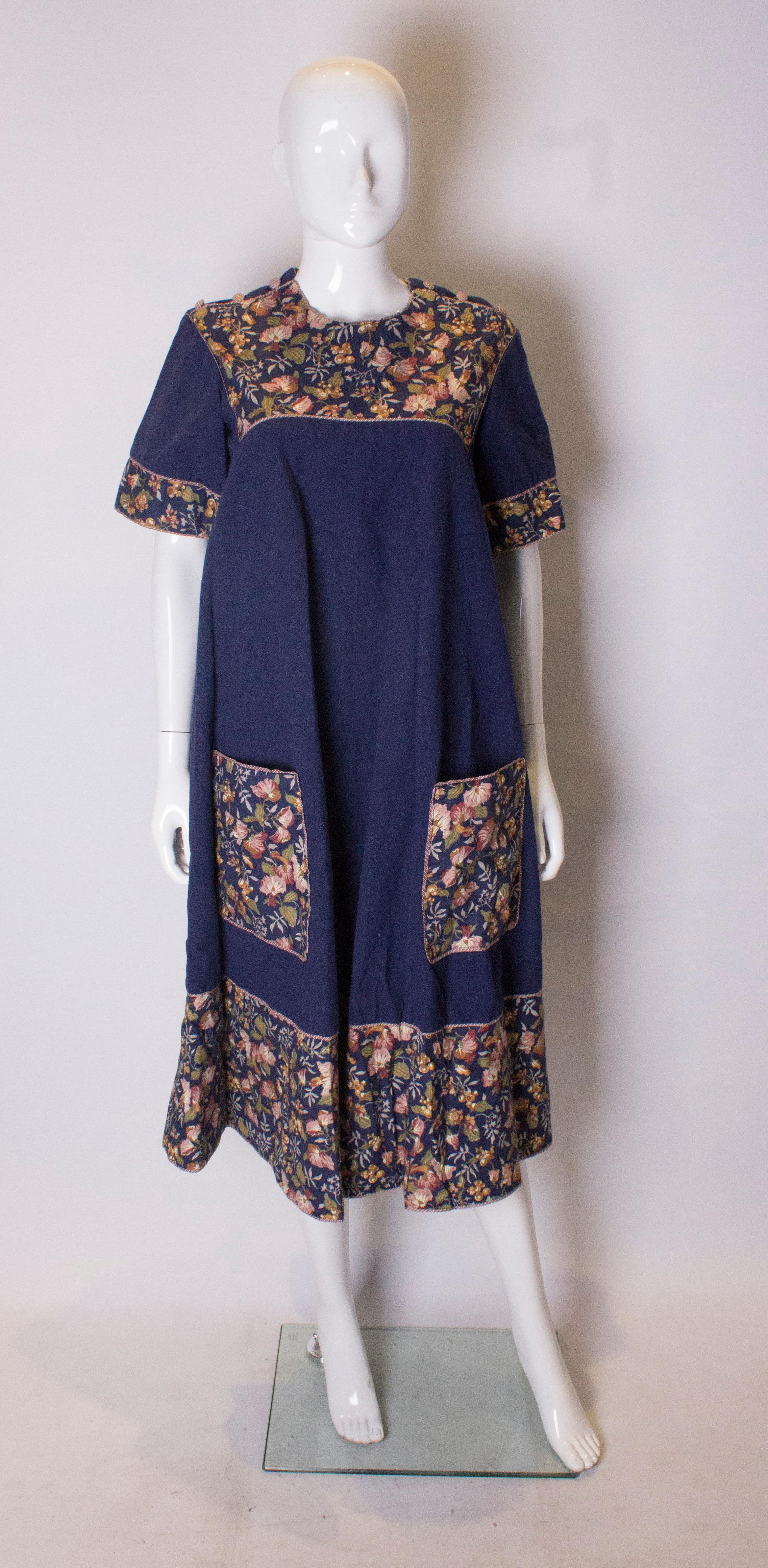 A pretty and easy to wear dress from Anna Belinda of Oxford. The dress is in a plain blue linen like fabric with floral print detail on the yoke , hem , pockets and sleeves. The dress opens via three buttons on each shoulder and the dress is fully