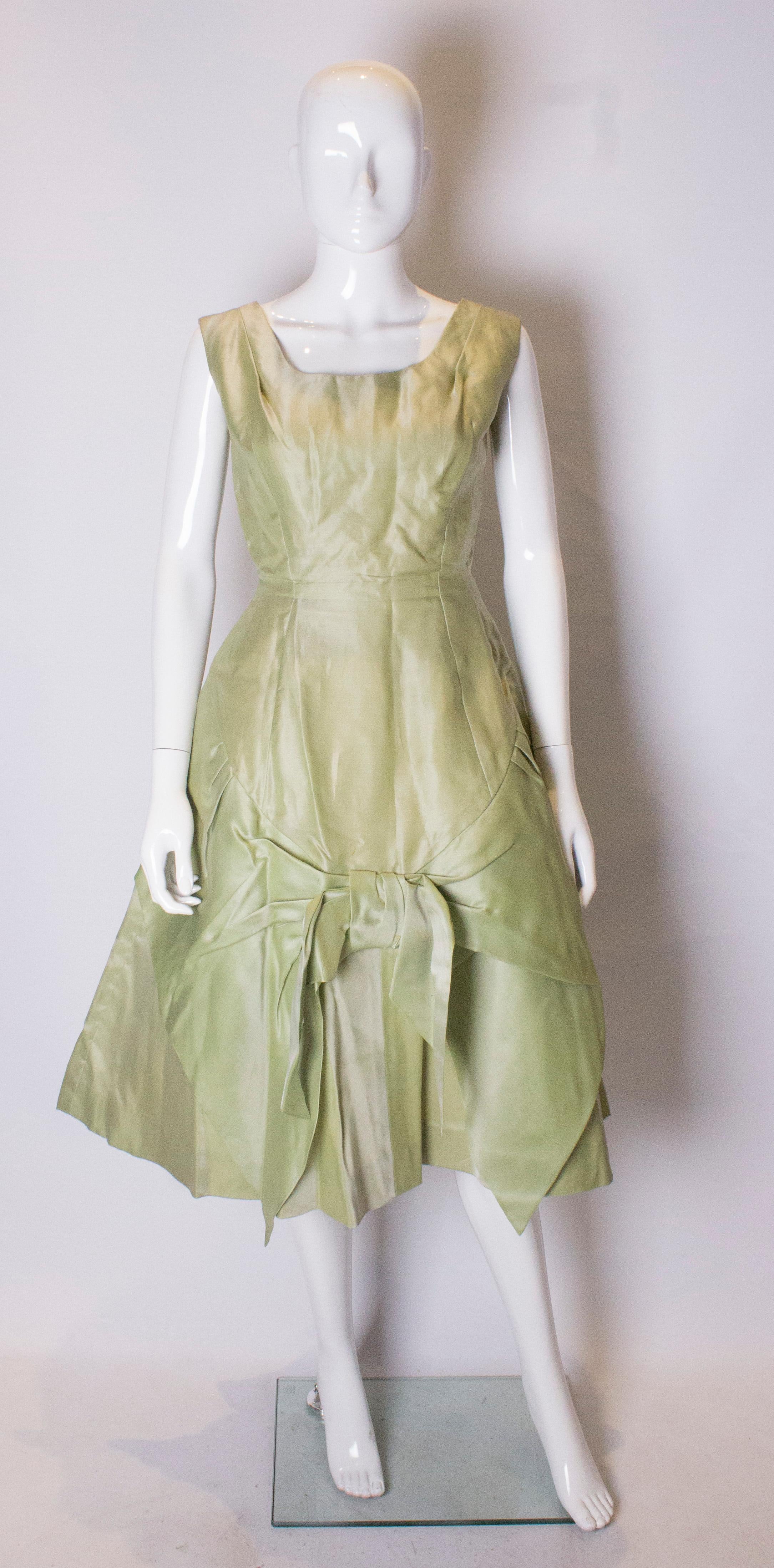 A pretty vintage cocktail dress by Cresta Couture . The dress is in a pistachio green colour and has a round neckline, full skirt with bow detail, central back zip and layers of petticoats.