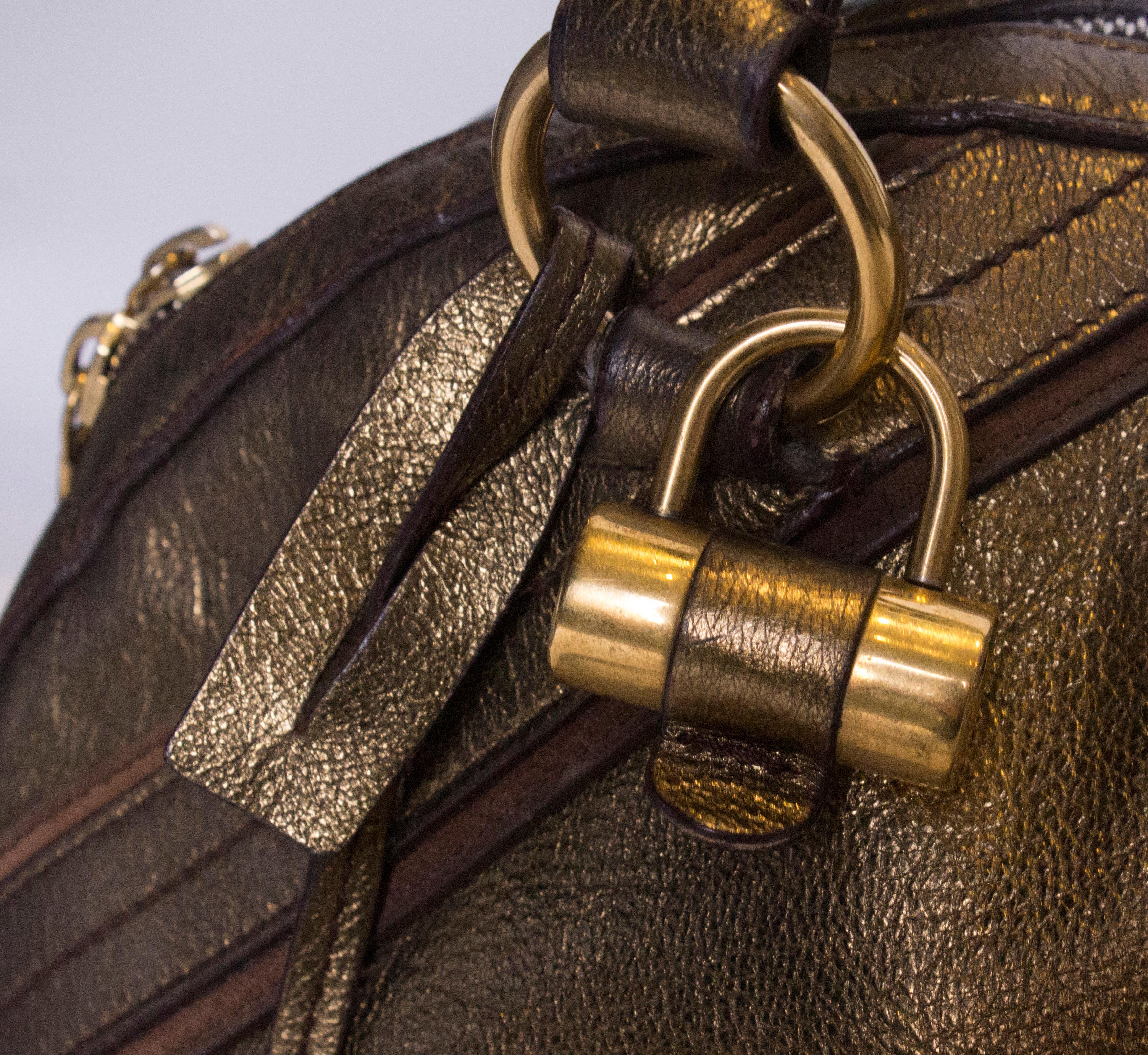 A great YSL Muse Bag in gold /bronze colured leather. The bag has a central top zip , with two handles and there is a detachable shoulder strap.Internally there is one zip pocket. The bag has the padlock and key.
Measuerments: width 17'' height 12''