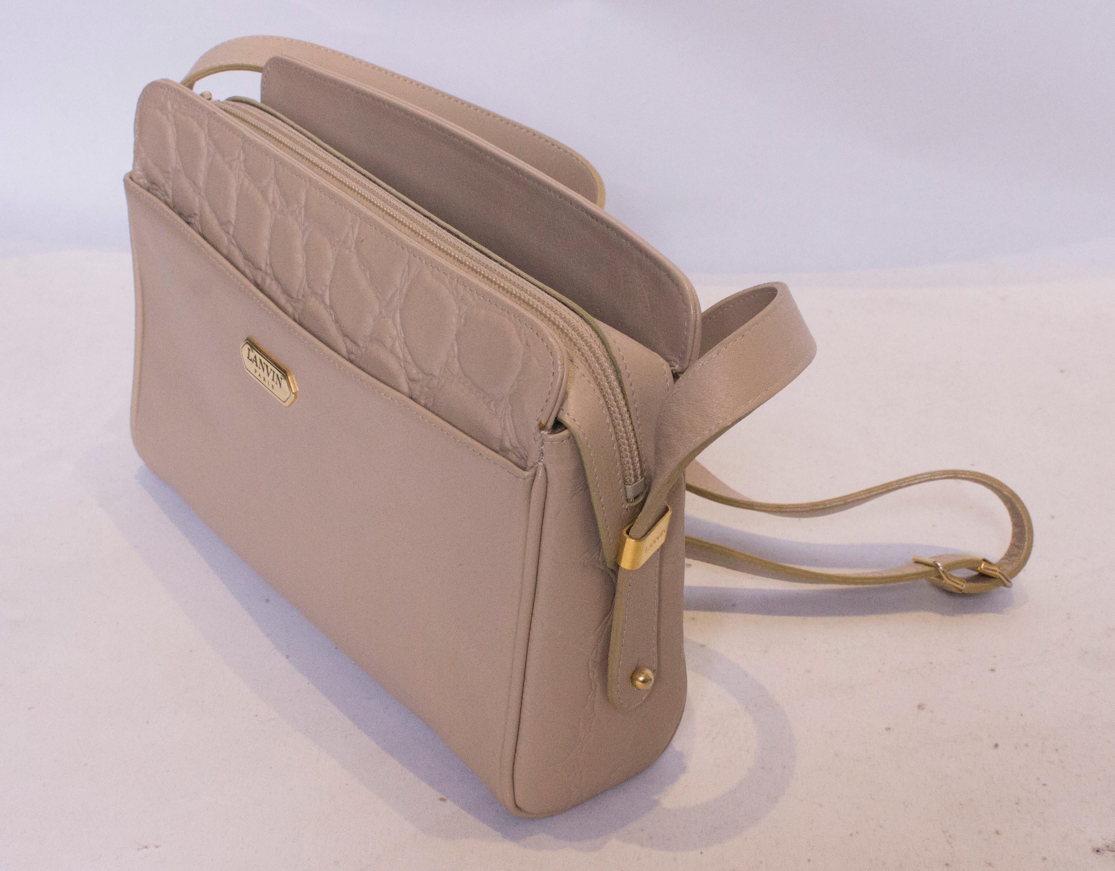 A chic leather handbag by Lanvin Paris. The bag is stone coloured , with a pouch on either side and one internal zip pocket. The bags has a stamped stone effect.