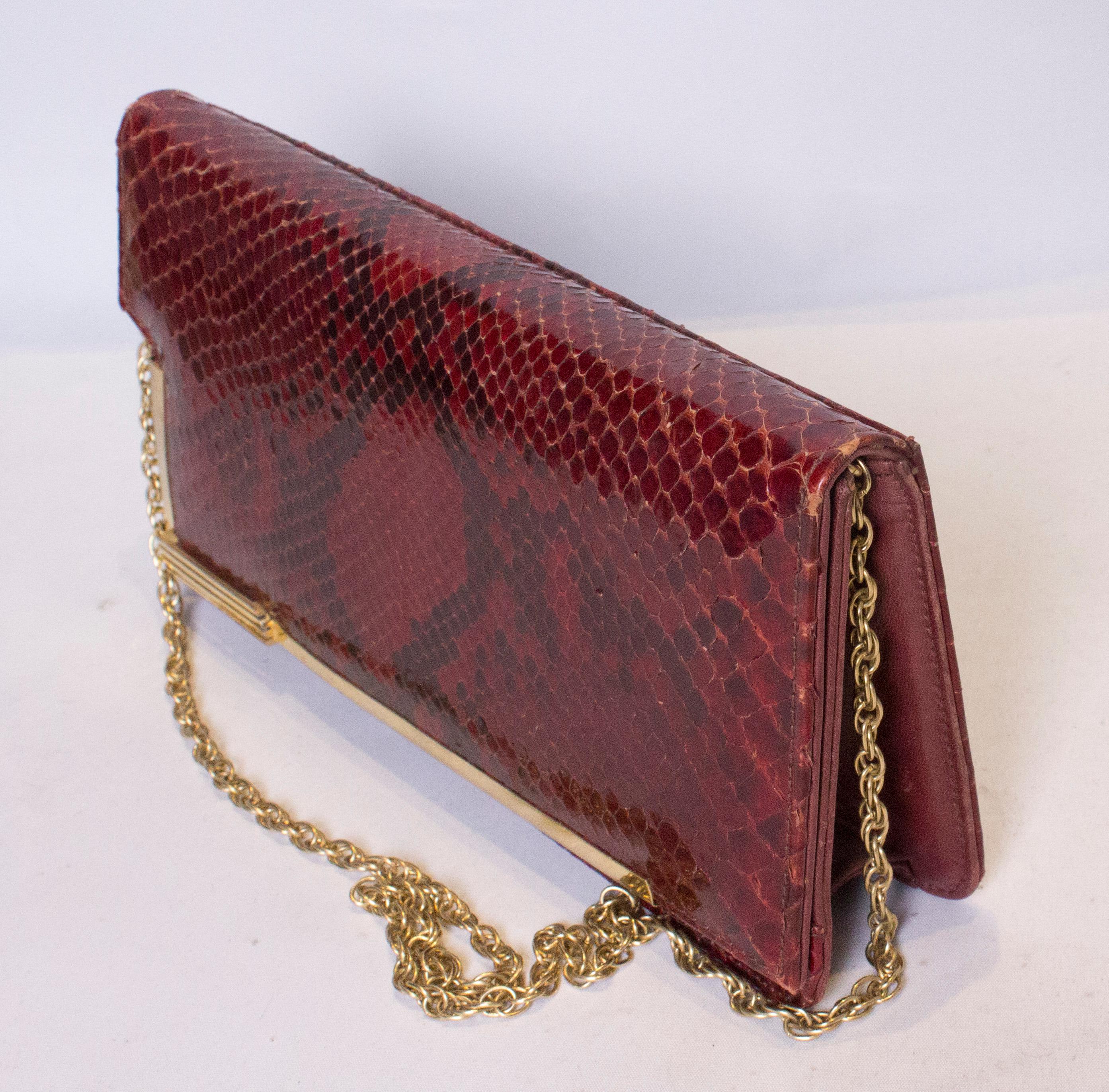 Un sac à main vintage chic en peau de serpent avec une garniture dorée et une poignée en chaîne.  Le sac se ferme à l'aide d'une fermeture à boutons-poussoirs et comporte une poche zippée à l'intérieur.
Mesures : largeur 11'', hauteur 6'',