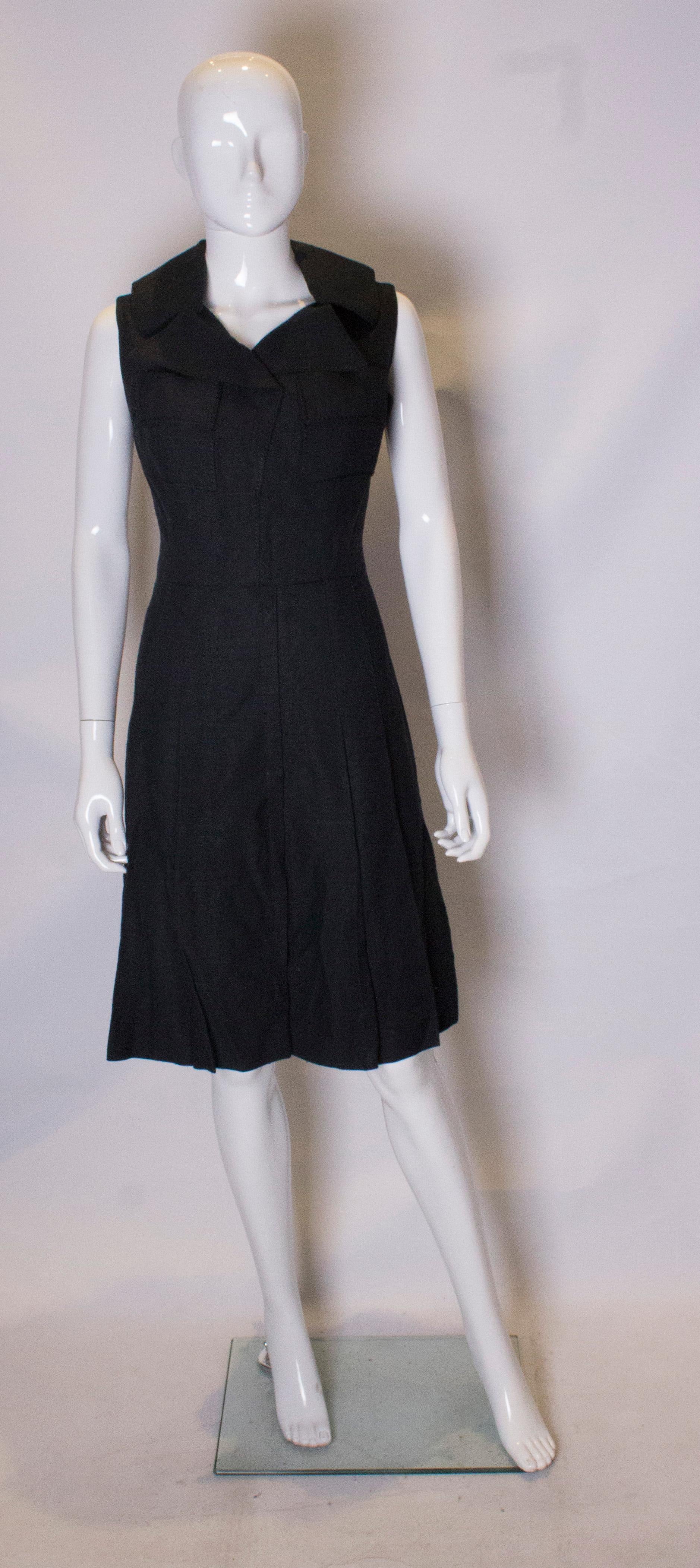 A chic black dress dating from the 1960s, from the Fashion Club London. The dress has a cut away collar, two breast pockets and a pleated skirt with pleats sewn in to hop leval. It has a central back zip and is fully lined.