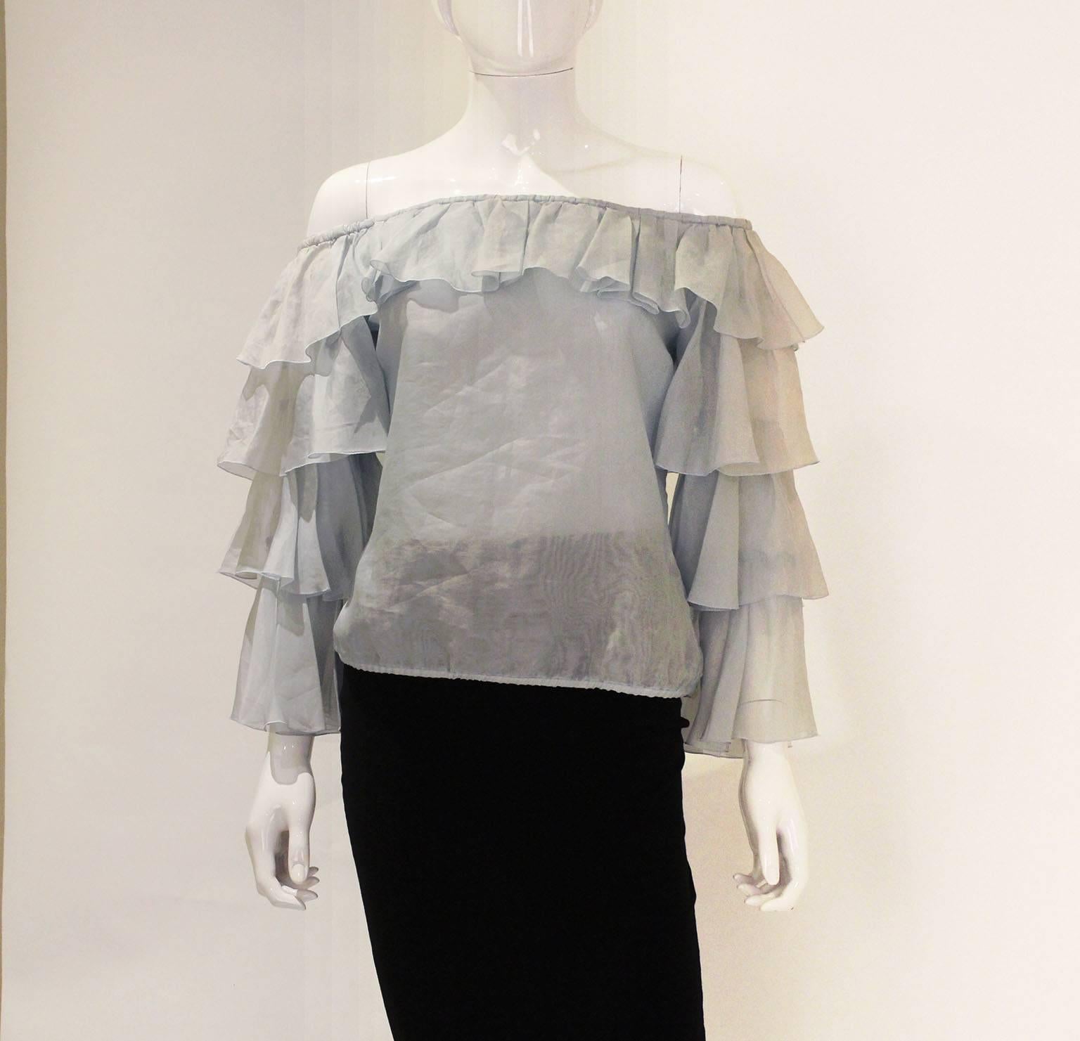 An enchanting silk blouse from the Italian designer Valentino. This blouse is in ice blue silk  with a ruffle elasticated neckline, and three tiers of silk on each sleeve. It has an elastic waist and a 5 button side opening on one side. 
It is