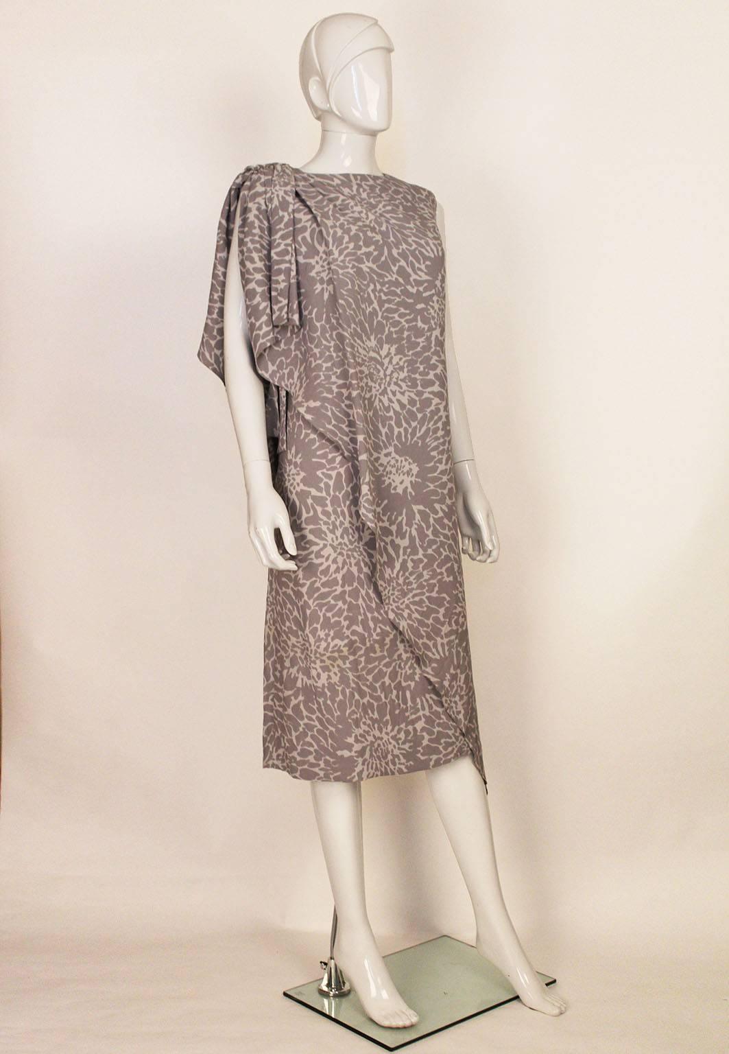 An elegant gown by Pierre Balmain,in a pretty grey and white print. The dress is sleeveless and has an interesting diagonal drape on the front and back.In addition the dress has a small waterfall drape on the shoulder.There is a back zip opening.