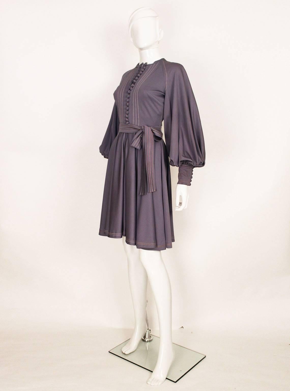 A charming and chic dress by British designer Jean Varon.  This dress is made of jersey, and is in a lovely light lavender colour . The dress has a button front down to the waist and a short zip from the waist down.The skirt is full and the  wide