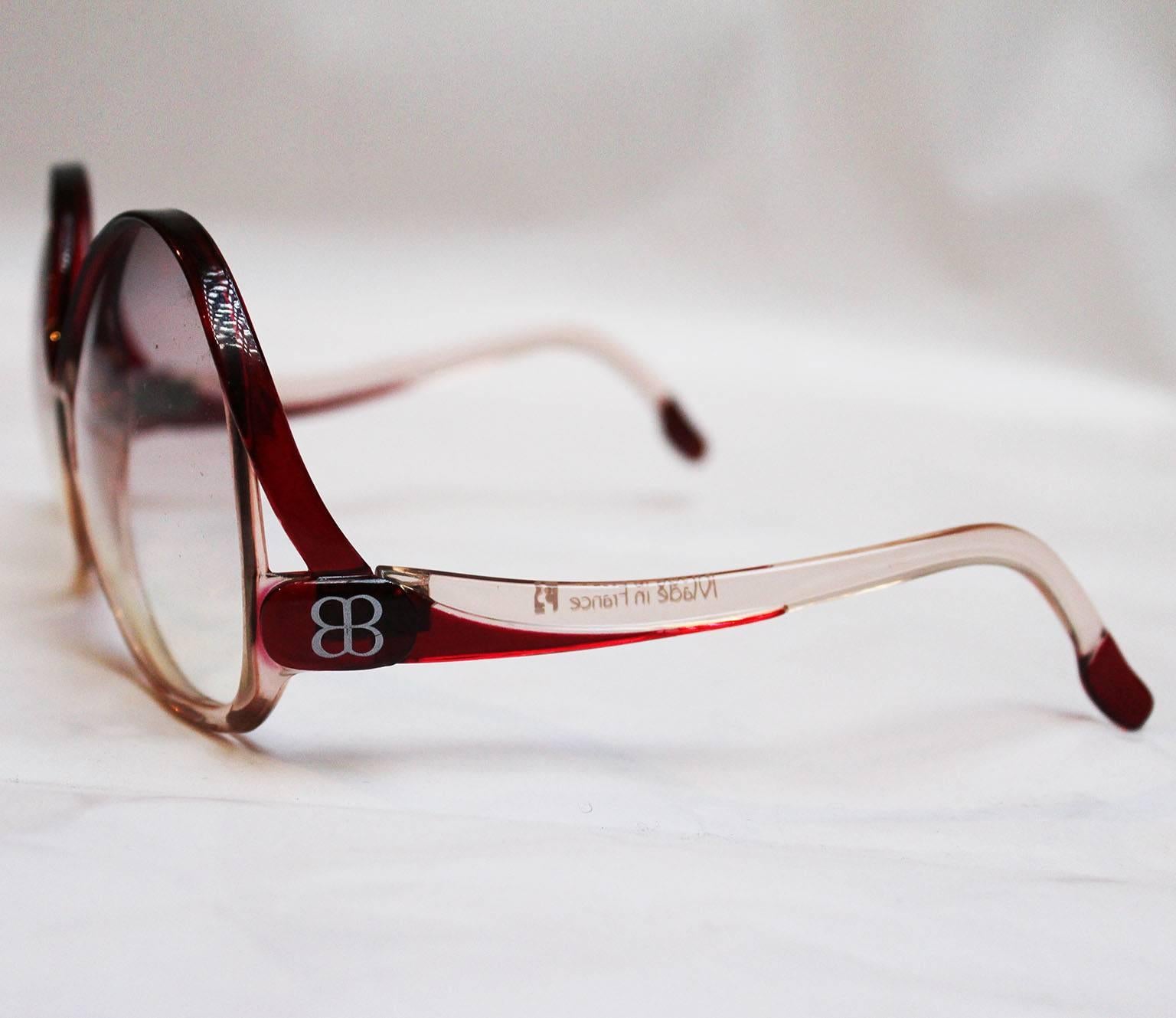 A great pair of groovy sunglasses by Balenciaga. These sunglasses have large butterfly lenses , with a deep red/burgundy frame at the top of the lens and a pale pink colour on the lower lens.The lower part of the arm is deep red/burgundy with a