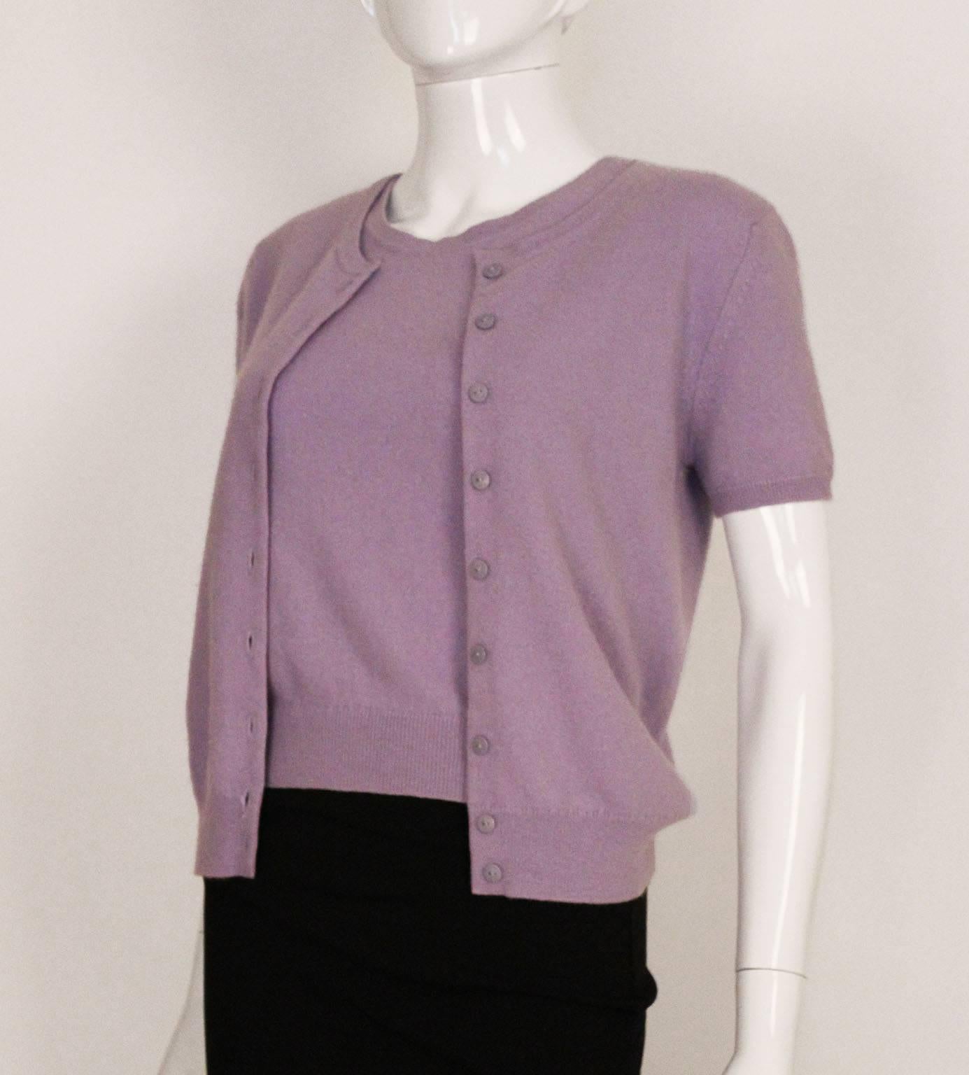 A charming and chic cashmere twinset by Chanel. In a lovely lavender colour, the twinset comprises, a shell top with round neck line, and a short sleeved cardigan with round neck .The cardigan has 9 buttons ,all stamped Chanel Paris.  Both items are