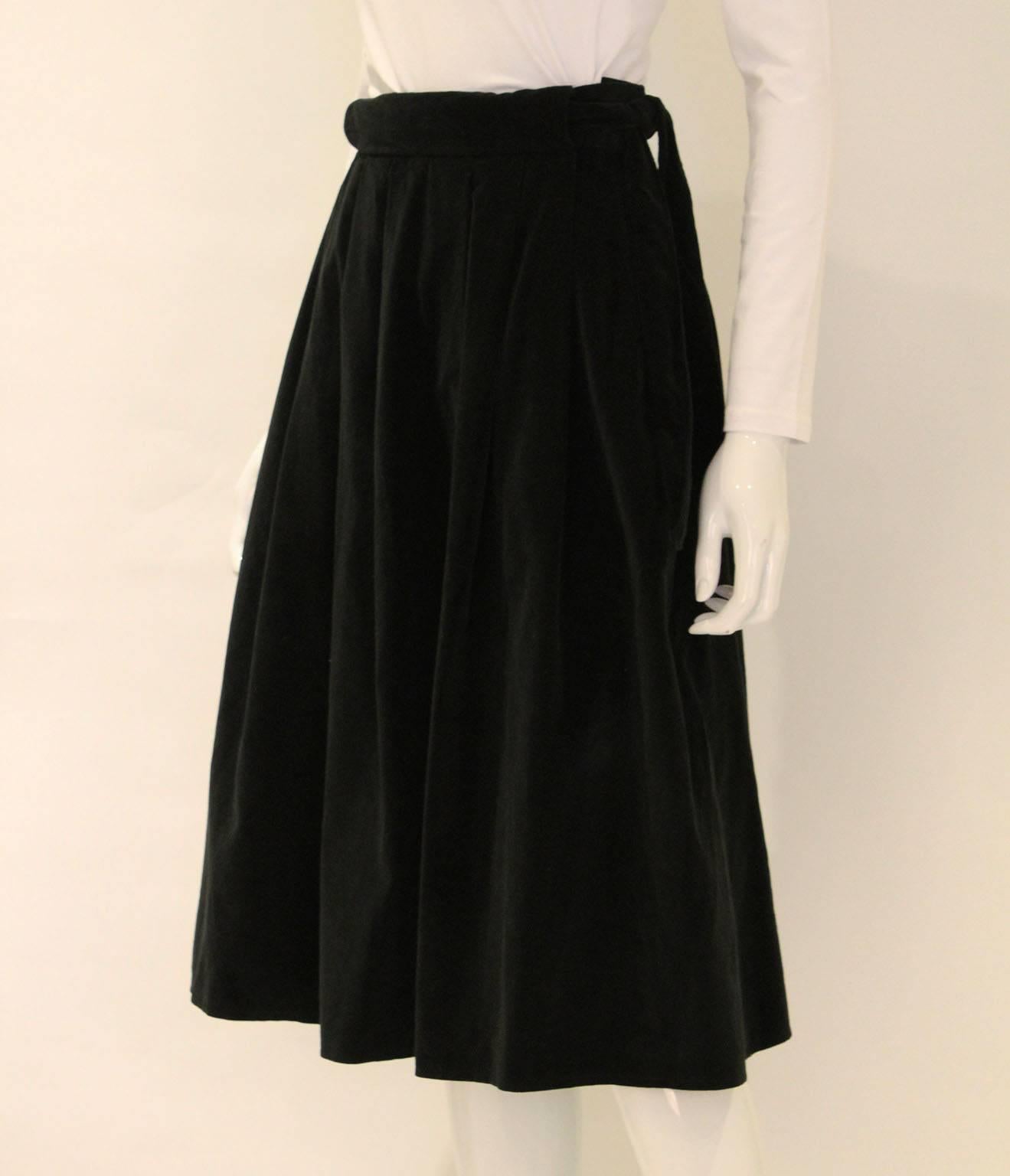A super skirt by Christian Dior, London. This black velvet skirt dates from the 1970s.It has  one central pleat with two pleats on either side on both  the front and back. There is a size zip fastening and button. In addition, there is a black