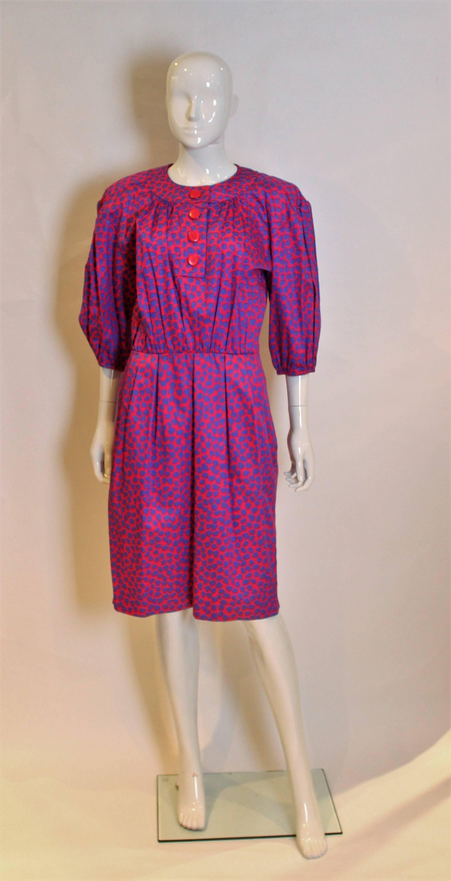 A great day dress by Yves Saint Laurent. This dress is in a satinised cotton,with purple hearts on a pink background.The dress is collarless with a four button opening , elbow length sleeves,a zip opening on the left hand side and pocket on the