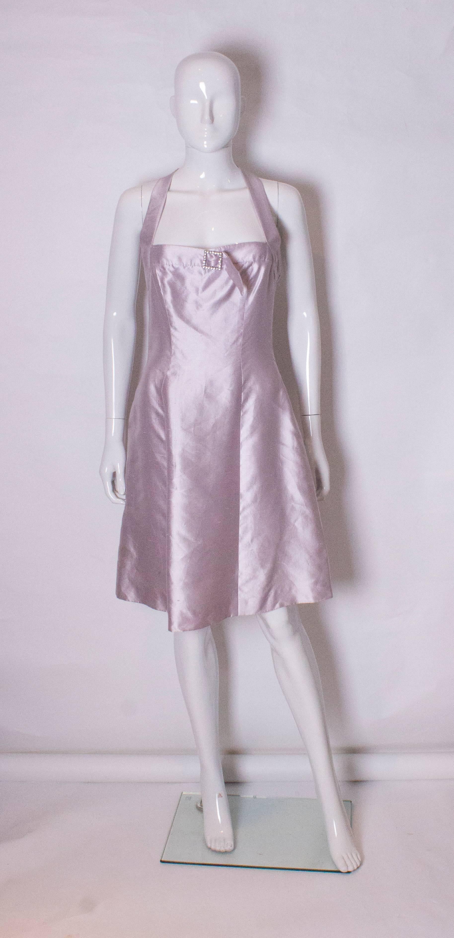 A chic cocktail dress by British designer Bruce Oldfield. The dress is in a pale lilac/ silver silk , and is fully lined. The dress has an interesting t detail at the back and a diamante buck on the bust.