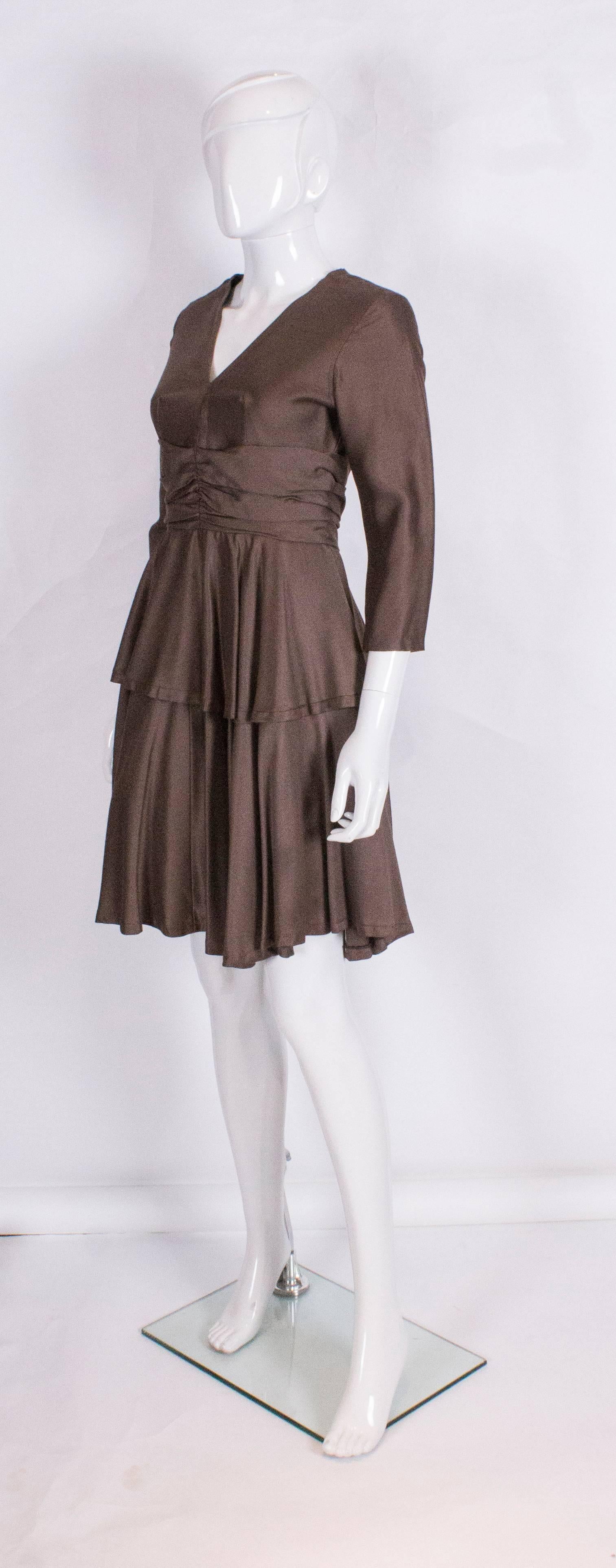 A chic cocktail dress by British designer Jane Varon.
The dress has a v neckline ,elbow length sleeves, a net underskirt, and peplum like detail.