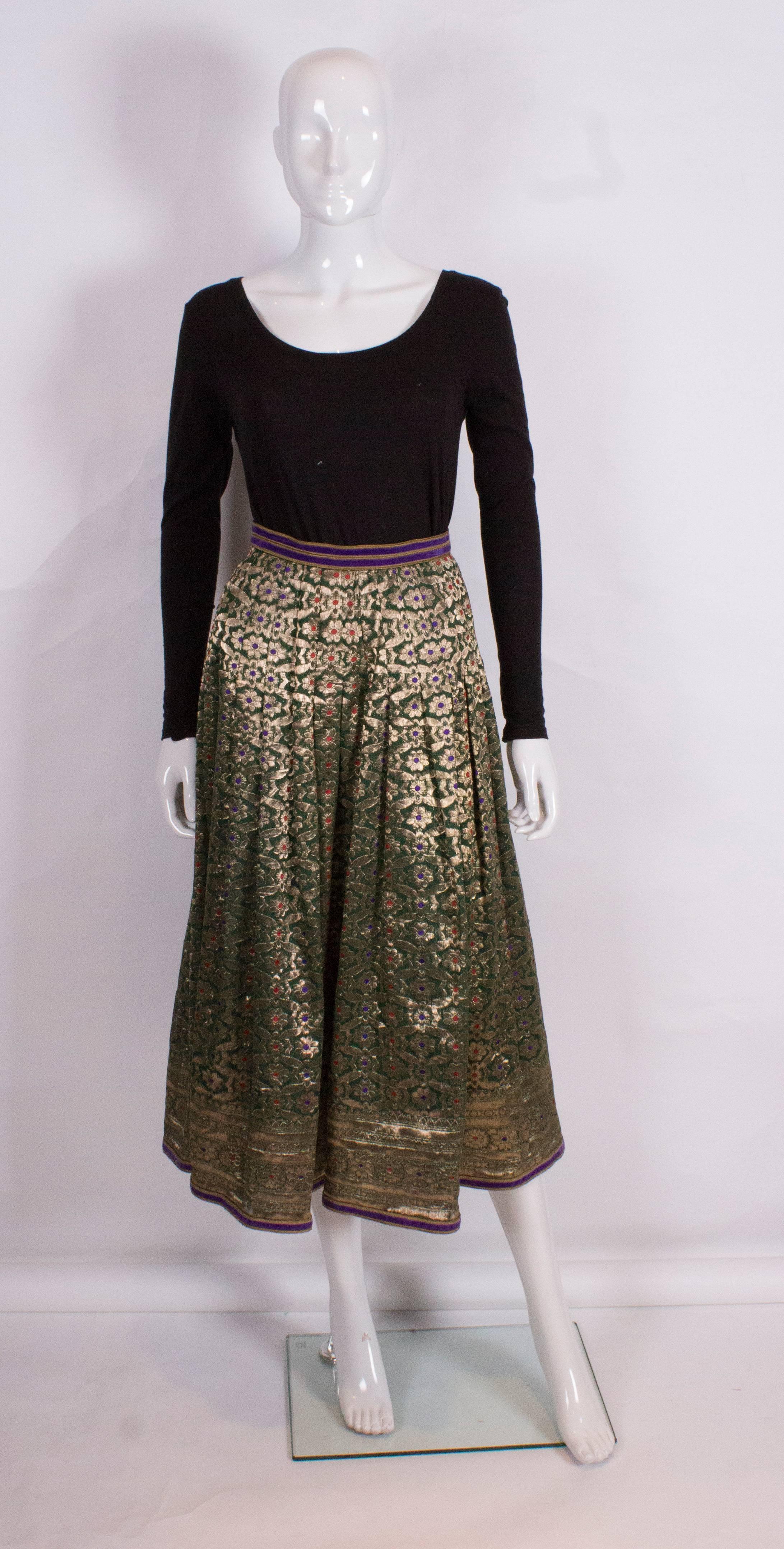 A stunning skirt for the party season from Regamus London.The skirt has a green background,with gold  , red and purple detail. The skirt has 5 1/2'' sewn down pleats from the waist band, and a 5 1/2''deep border at the hem. The skirt has a zip