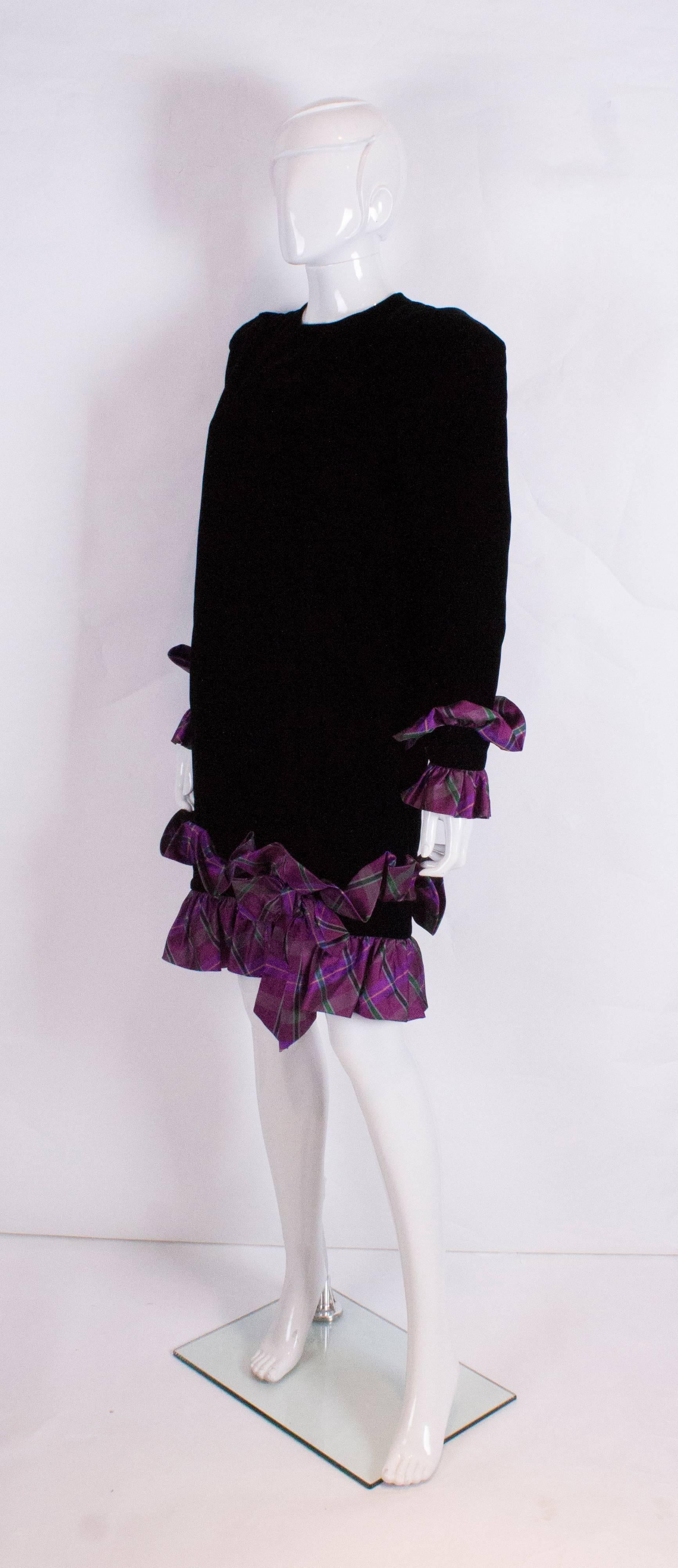 A chic dress by Italian designer Juditte. The body of the dress is black velvet and the lilac tartan frills are on the hem and cuffs. The cuffs have two buttons and there is  a button opening at the back of the dress.