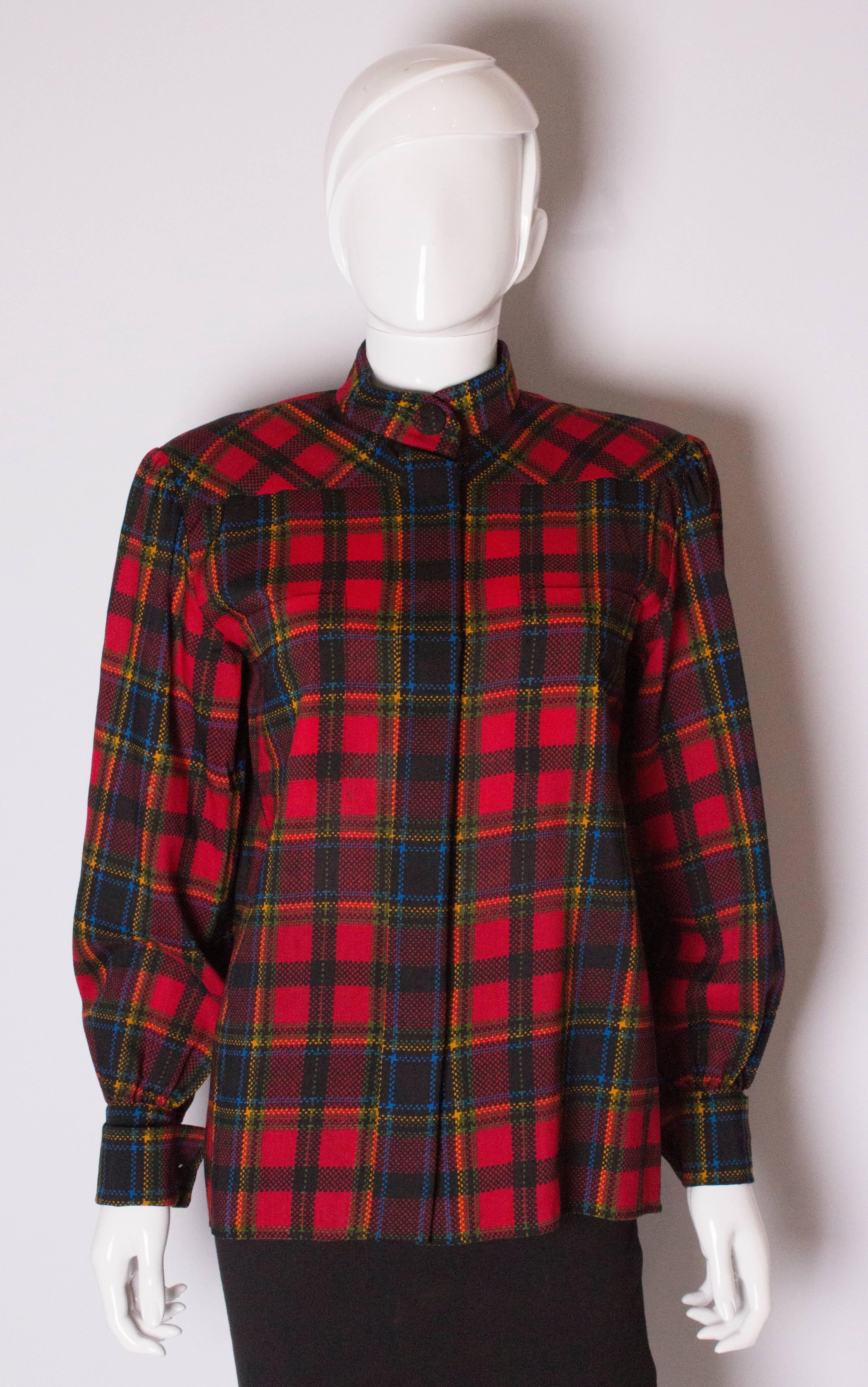 A great blouse for the festive season from Yves Saint Laurent, Rive Gauche line. The blouse has a red background , with red, blue, green and yellow lines. It has a stand up collar, one button fastening at the neck , 6 hidden button fastenings at the