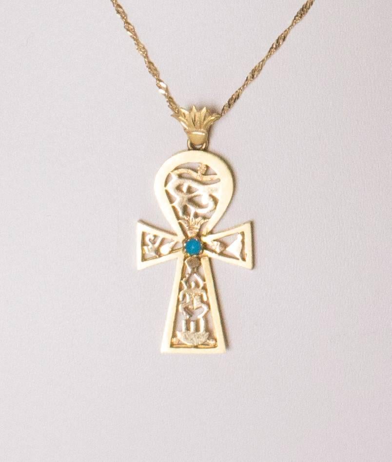 Una cadena de eslabones de oro que mide 16'', con una cruz de oro que mide 1 1/2'' por 3/4'', y tiene una piedra turquesa en el centro.