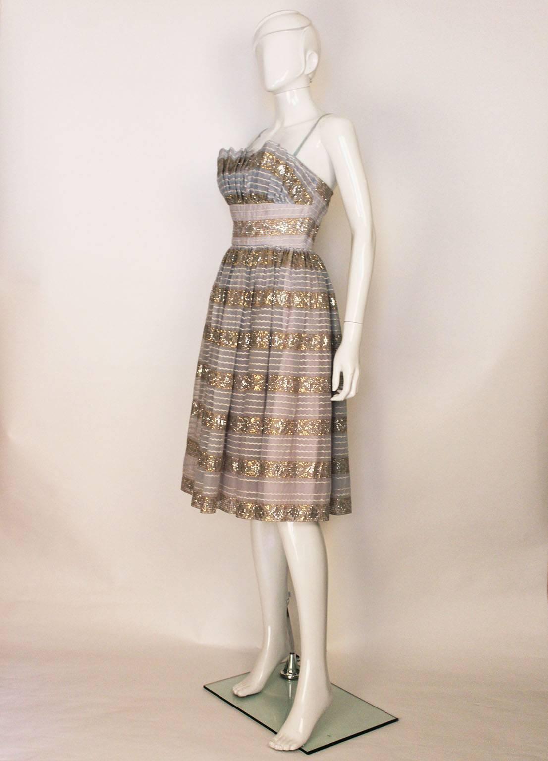A chic cocktail/evening dress by Victor Josselyn. In a pale blue fabric with gold and silver decoration, plus white horizontal braiding, this dress is a great party piece. It has spaghetti straps,  a full skirt and is fully lined.