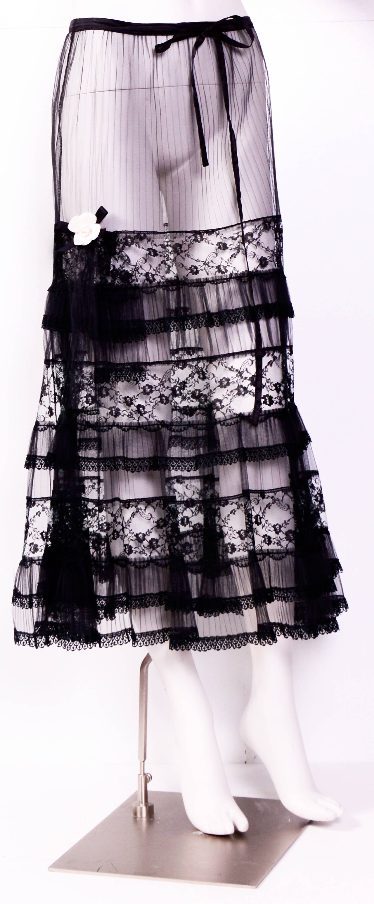 Chanel Camellia Off White Flower Black Ribbon Pin Brooch attached to this adorable Lace & Tulle ruffle skirt. 
Black tulle mini pleats trimmed with lace, 2 attached lace and tulle panels on the side. Silk ribbon drawstring at the waist but no
