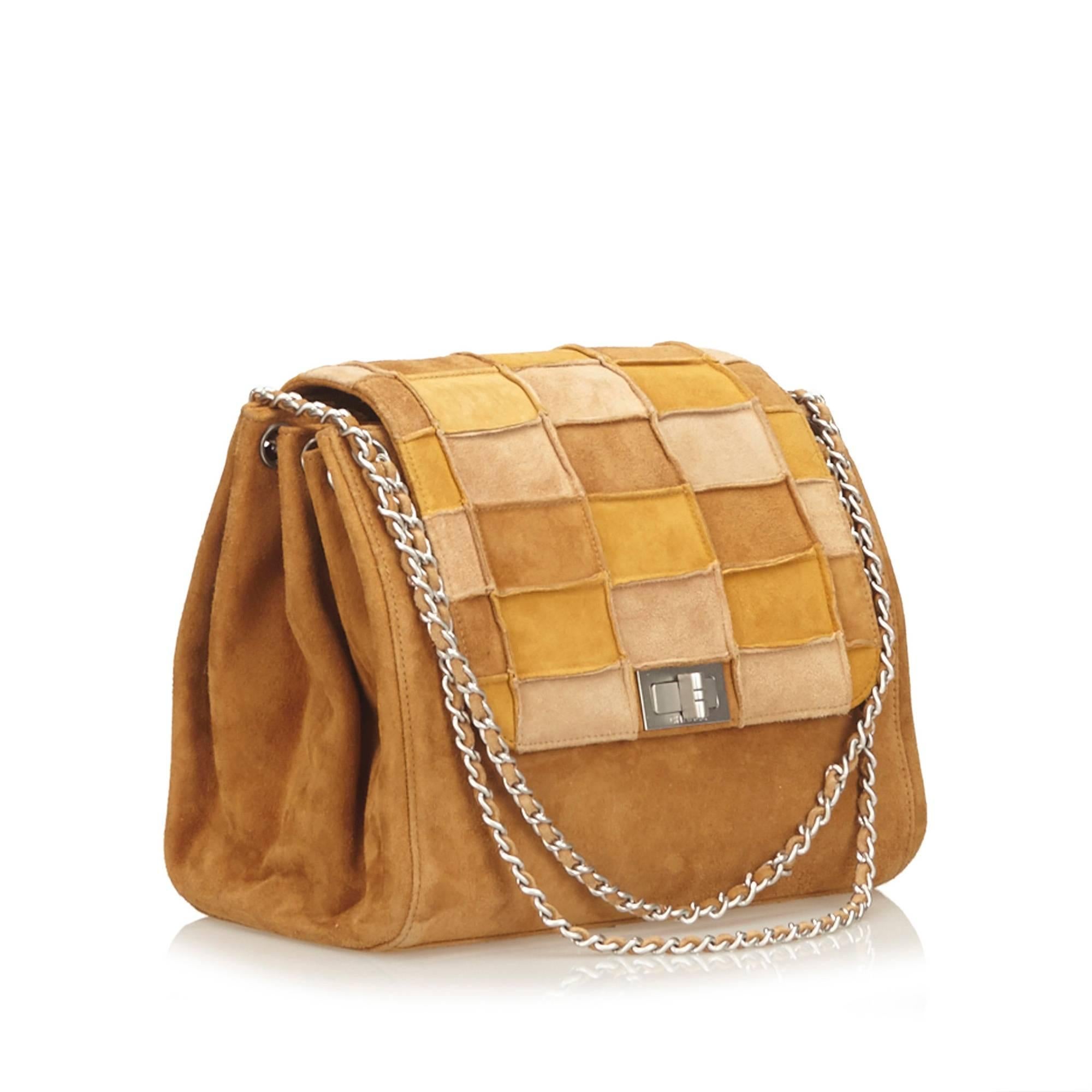 This shoulder bag features a chain strap, a patchwork front flap with a twist lock closure, and an interior zip pocket.