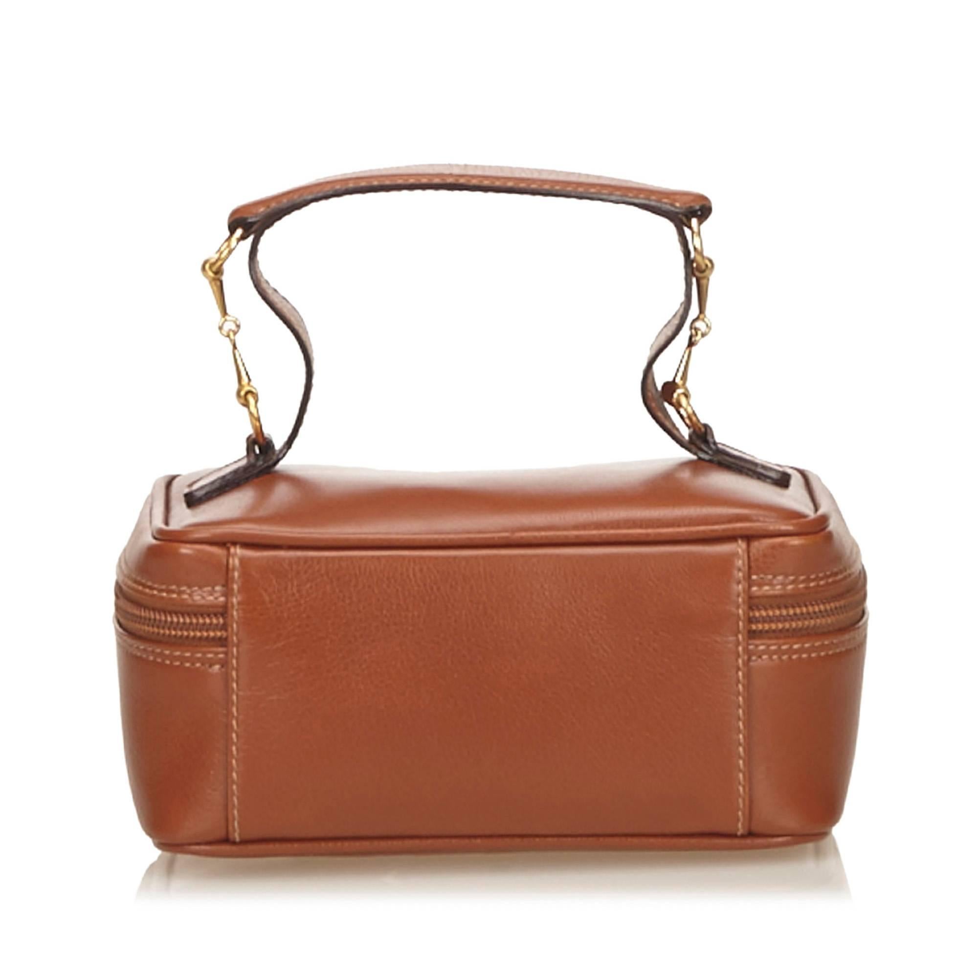 This vanity bag features a leather body, a top handle with gold-tone horse bit hardware, and a top zip around closure.

Color: Brown