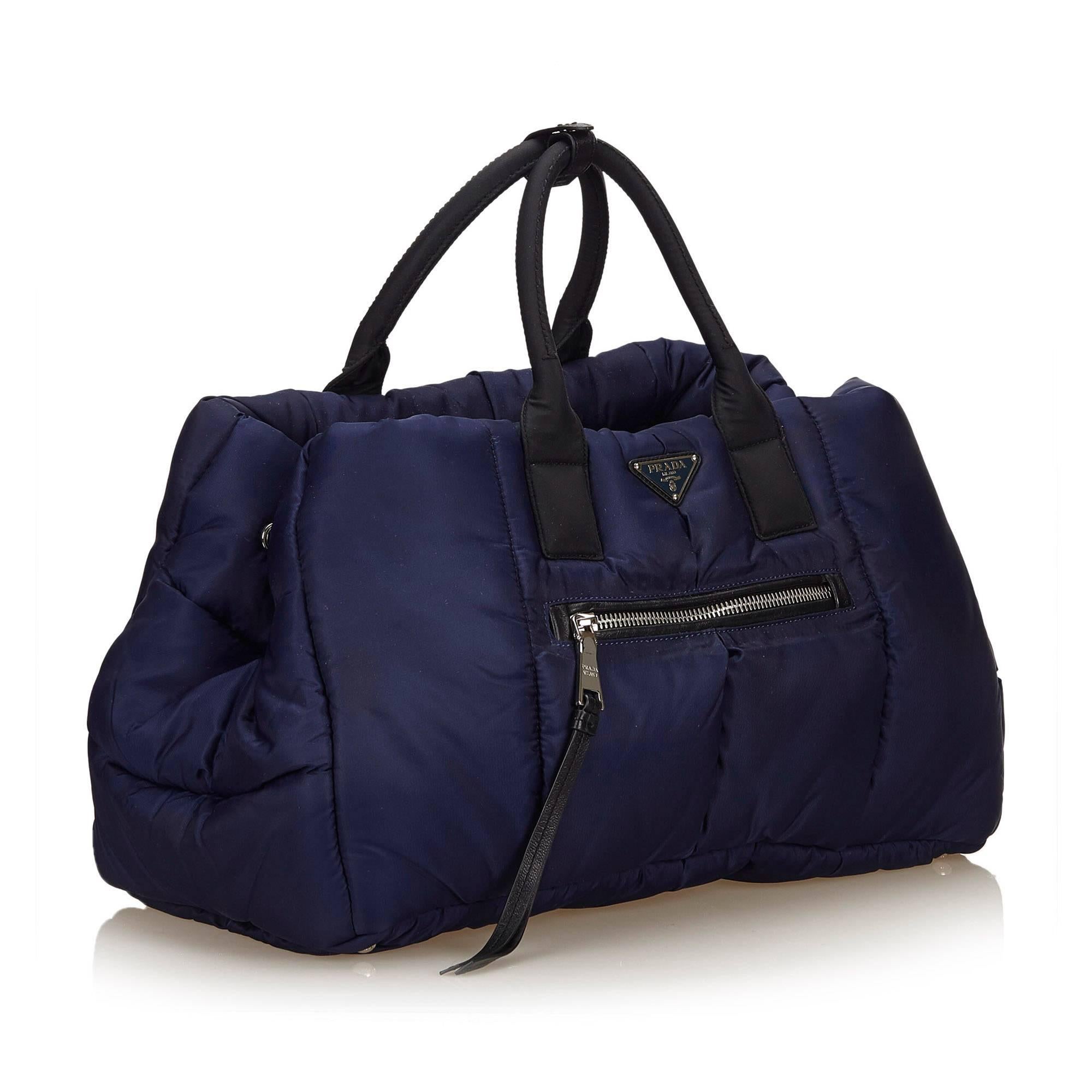 This handbag features a nylon body, exterior front and back zip pockets, rolled handle, open top, and interior pockets. 

It carries a B condition rating.

Dimensions: 
Length 27 cm
Width 43 cm
Depth 20 cm
Hand Drop 15 cm

Inclusions: Shoulder