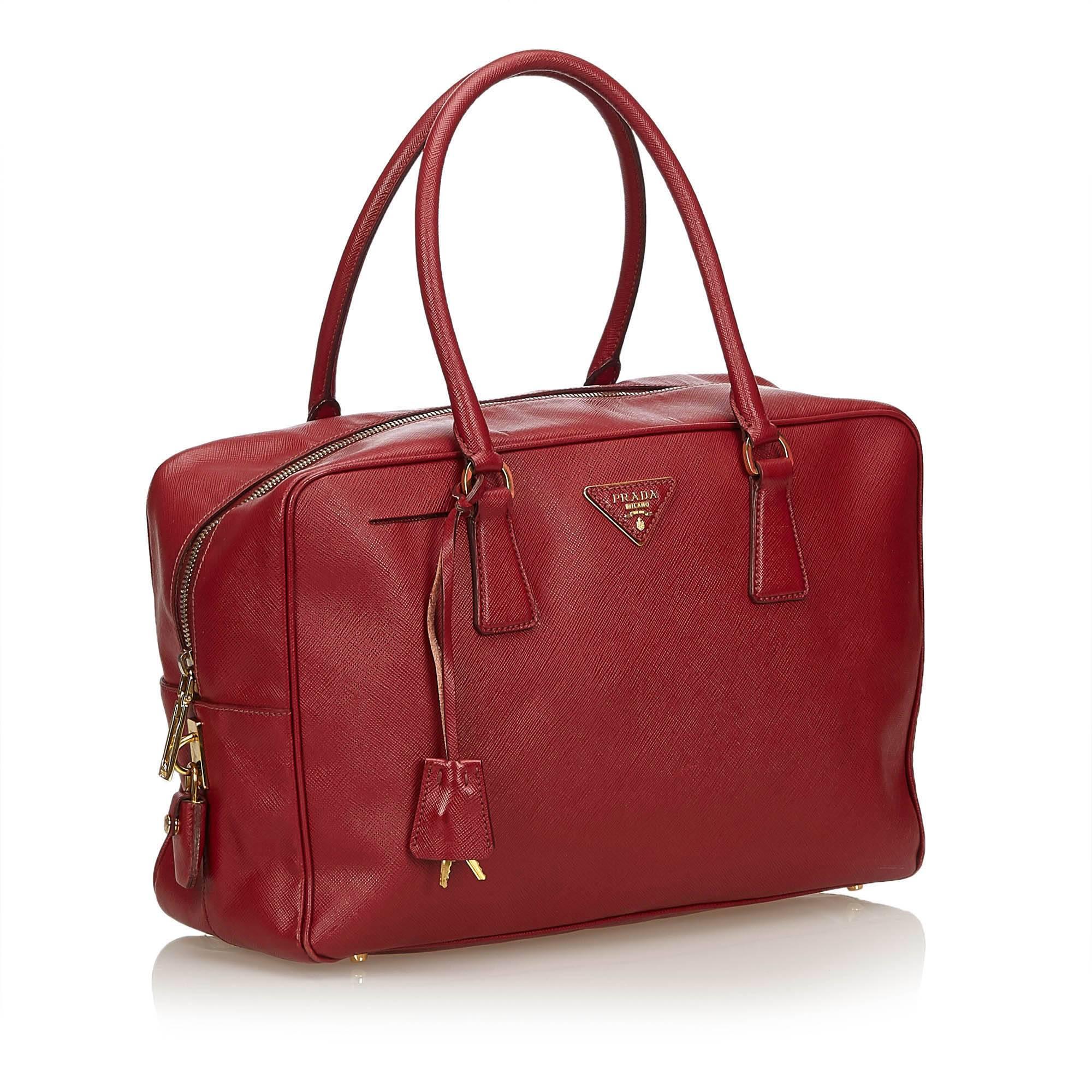 This bag features a leather body, rolled handles, top zip closure, and interior zip pocket. 

It carries a B+ condition rating.  

Dimensions: 
Length 23 cm
Width 34 cm
Depth 12 cm
Drop 17 cm

Inclusions: Padlock

Color: Red

Material: Leather x