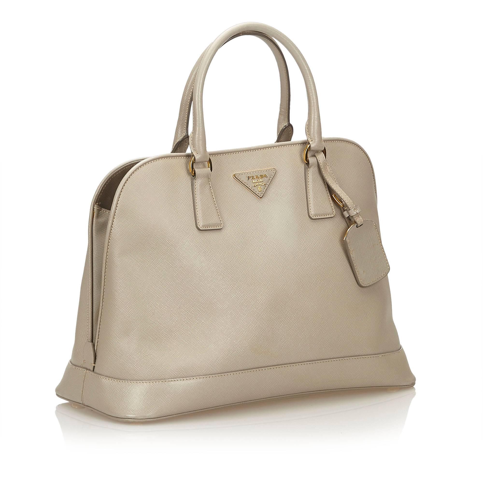 This handbag features a saffiano leather body, rolled leather handles, zip around closure, and interior zip compartment.

It carries a B+ condition rating.

Dimensions: 
Length 26 cm
Width 36 cm
Depth 16 cm
Hand Drop 13 

Inclusions: Name