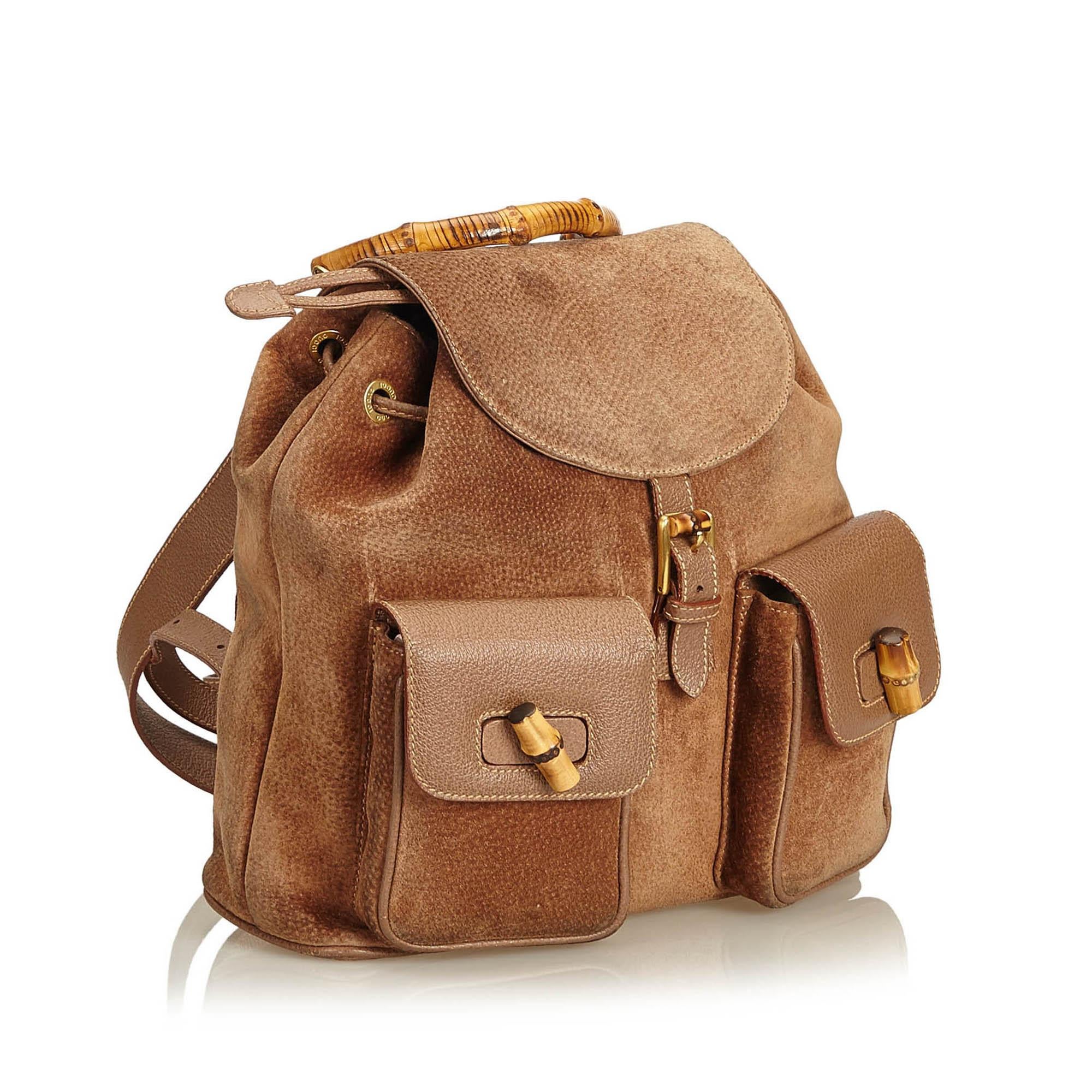 This backpack features a suede body, flat leather back straps, bamboo top handle, top flap with magnetic closure, drawstring closure, exterior flap pockets with bamboo twist lock closure, and an interior zip pocket.

It carries a B condition