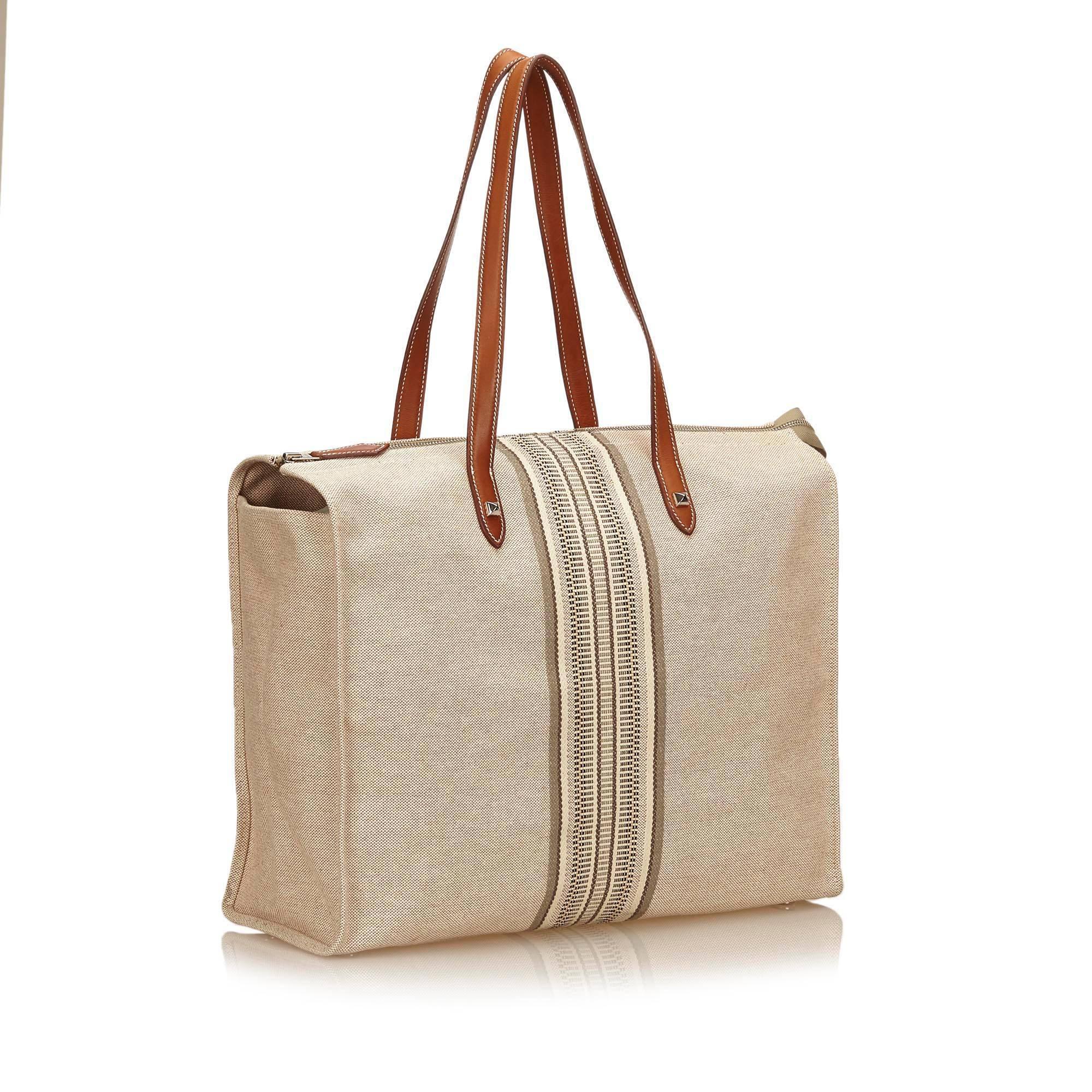 This shoulder bag features canvas body, flat leather handles, top zip closure, and interior open pocket. It carries a B condition rating.

Inclusions: 
Dust Bag