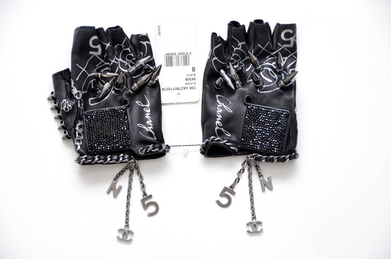 Chanel Gloves – Lambskin gloves with studs and the words “THE LITTLE BLACK GLOVES” written on the palm.
These unique and rare glove have it all:crystals,cc and 5 charms,chains and spikes.Gunmetal tone hardware.
From 2013 collection.New with tags