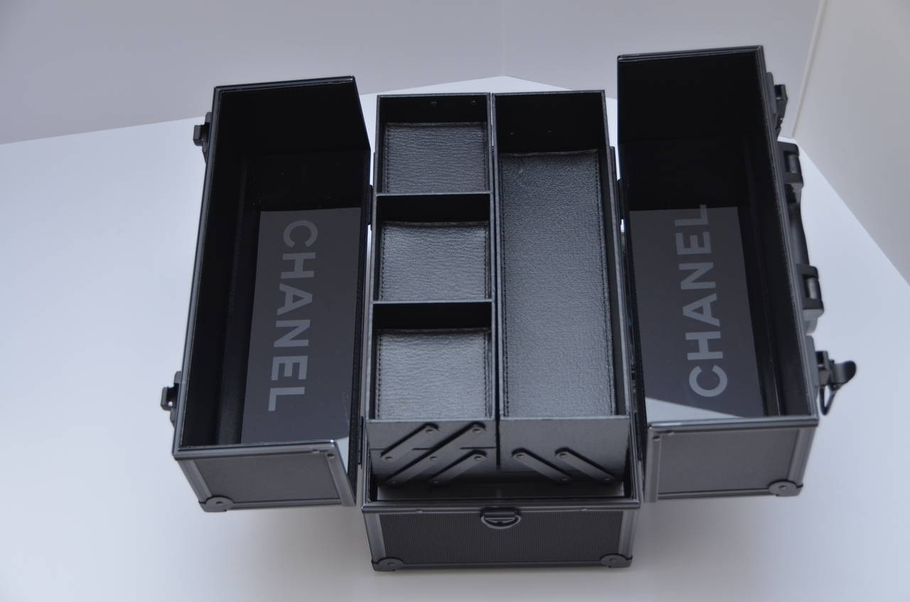 Black Chanel aluminum cosmetic case with tonal metal and resin hardware, logo placard at front, top handle, expandable interior trays with five compartments, leather trim, logo mirrors and latch closure. 
Includes three slotted inserts still