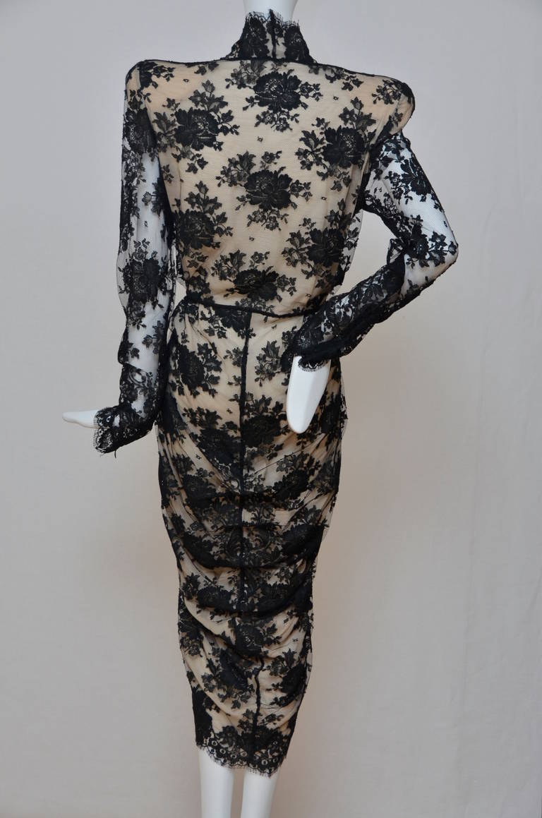 Black lace wrap front dress. The scalloped edged v-neck leads into a wrap front. Flesh colored silk lining. 
Pleat details sit on the high waist. Long sleeves. The dress drapes to the hemline that falls below the knee.
This beautiful lace wrap