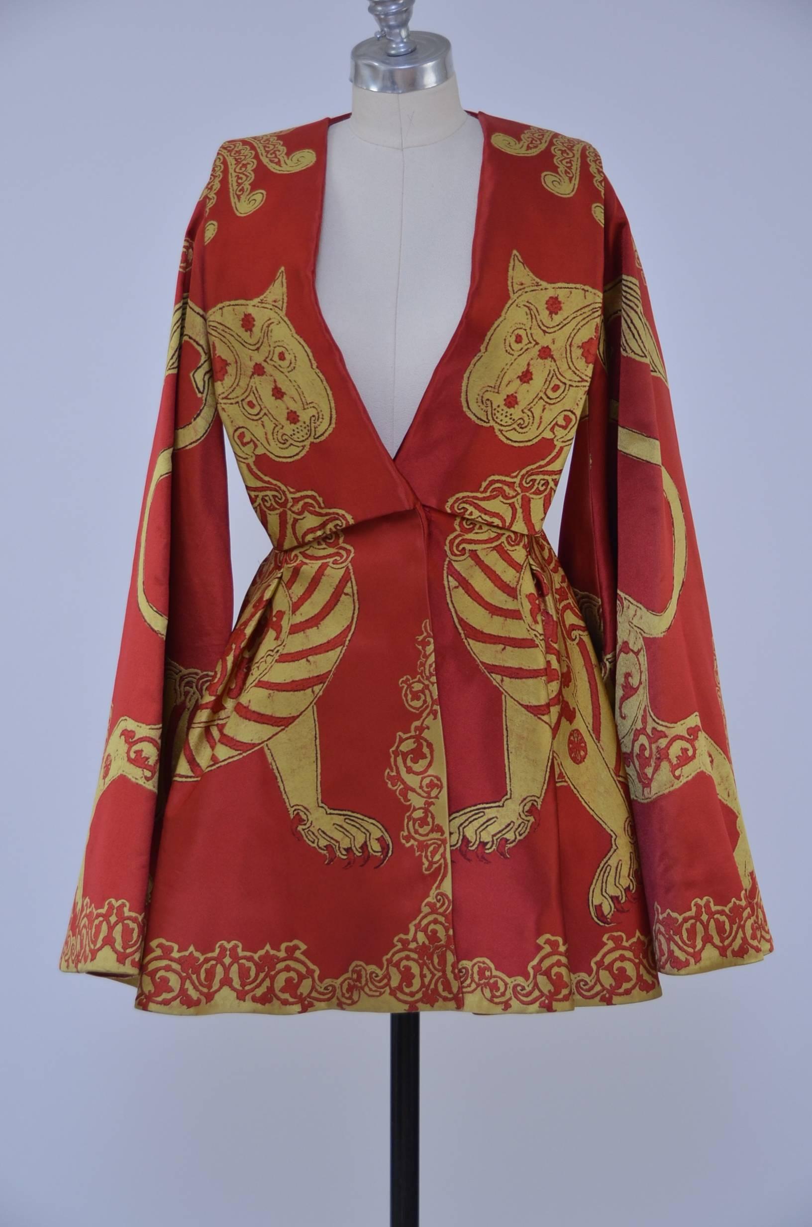 A fine Alexander McQueen cape dress. one of the sixteen designs made for his final collection from  Autumn-Winter, 2010.
Heavy scarlet and yellow gazar, woven with heraldic beasts, the wide gothic sleeves attached to the lower skirt