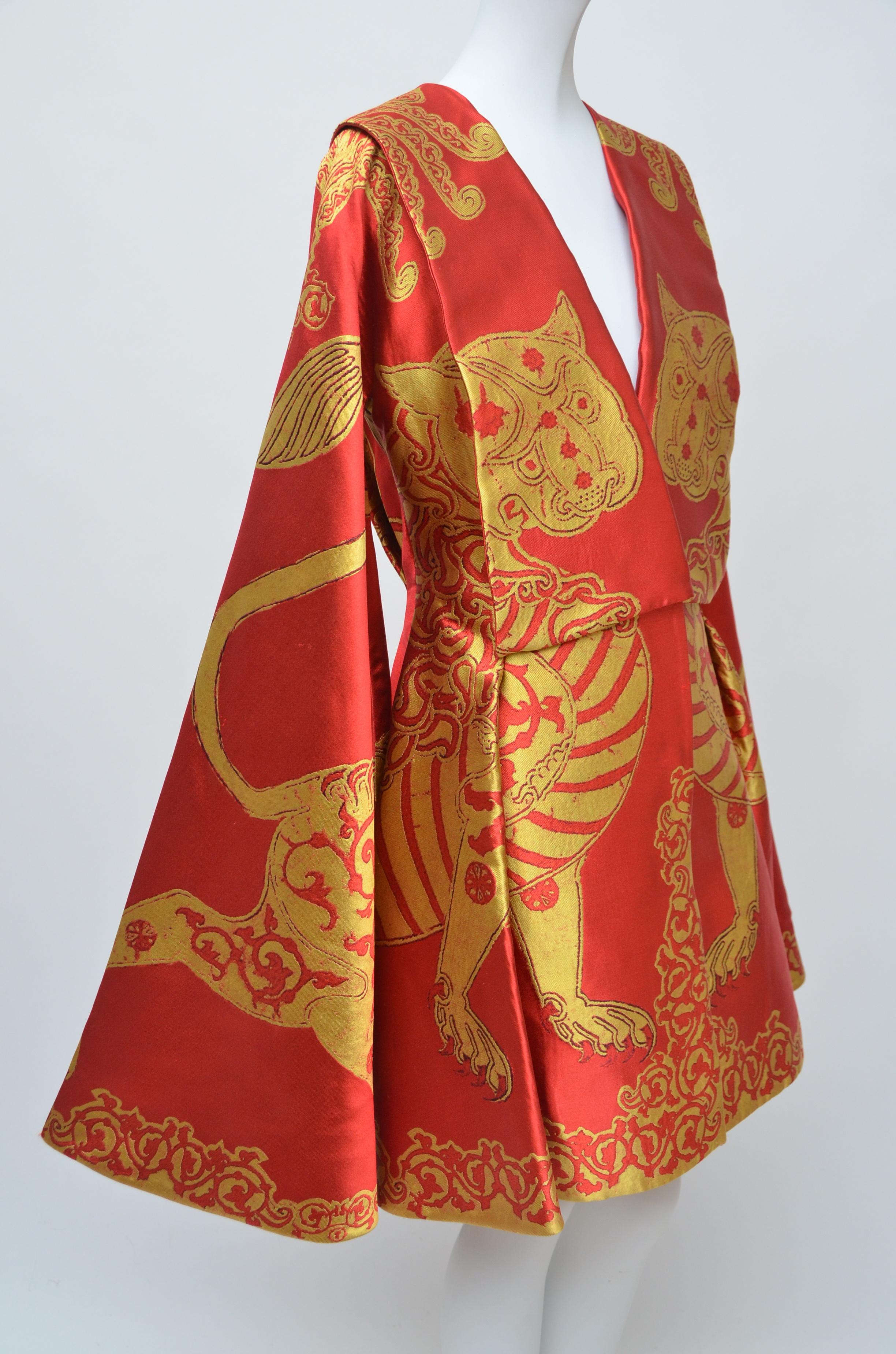 A fine Alexander McQueen cape dress. one of the sixteen designs made for his final collection from Autumn-Winter, 2010. 
Heavy scarlet and yellow gazar, woven with heraldic beasts, the wide gothic sleeves attached to the lower skirt sides.