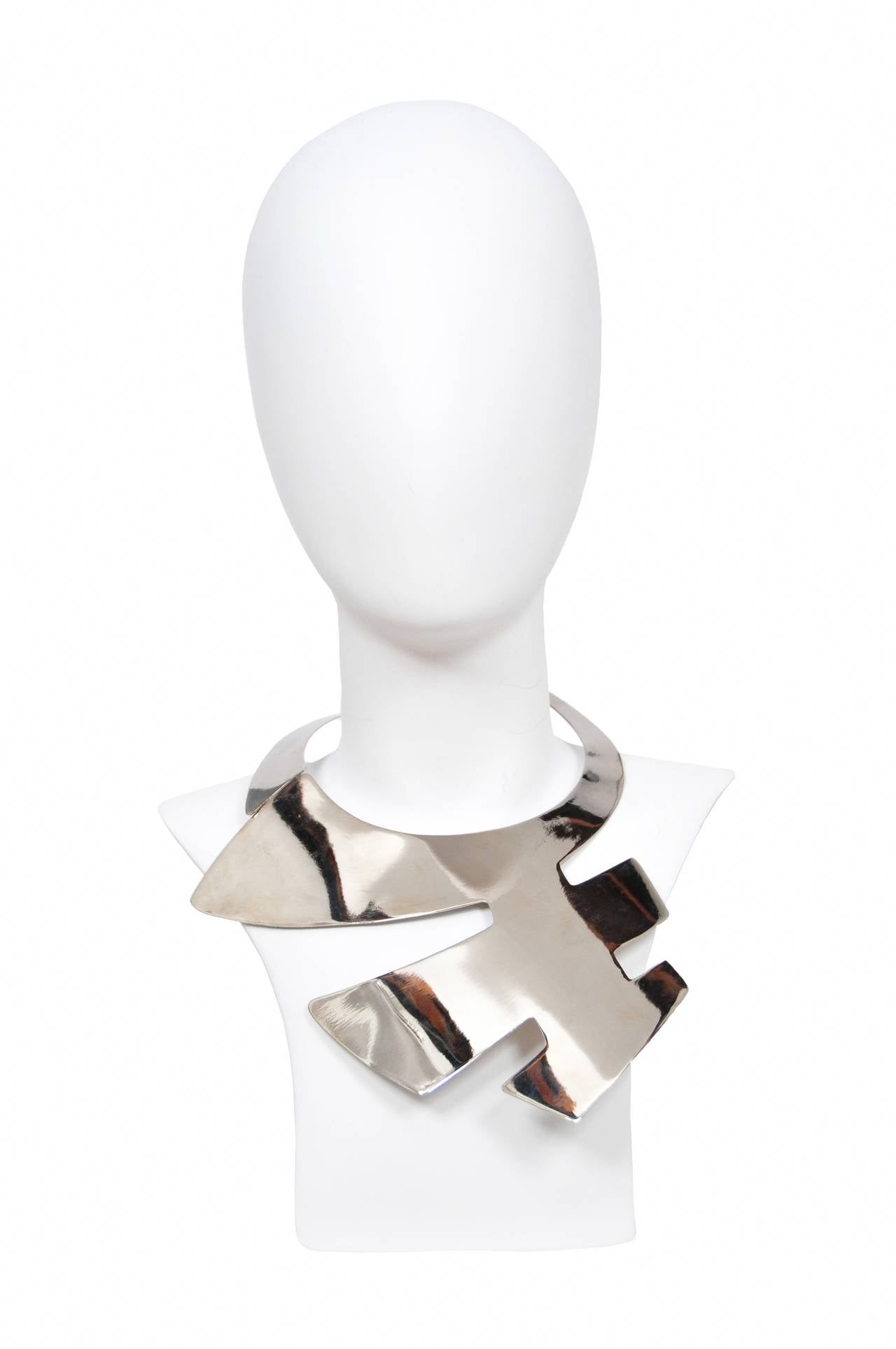 Pierre Cardin Iconic metal plate necklace with rounded geometric cut. Silver chain closure secures at neck.