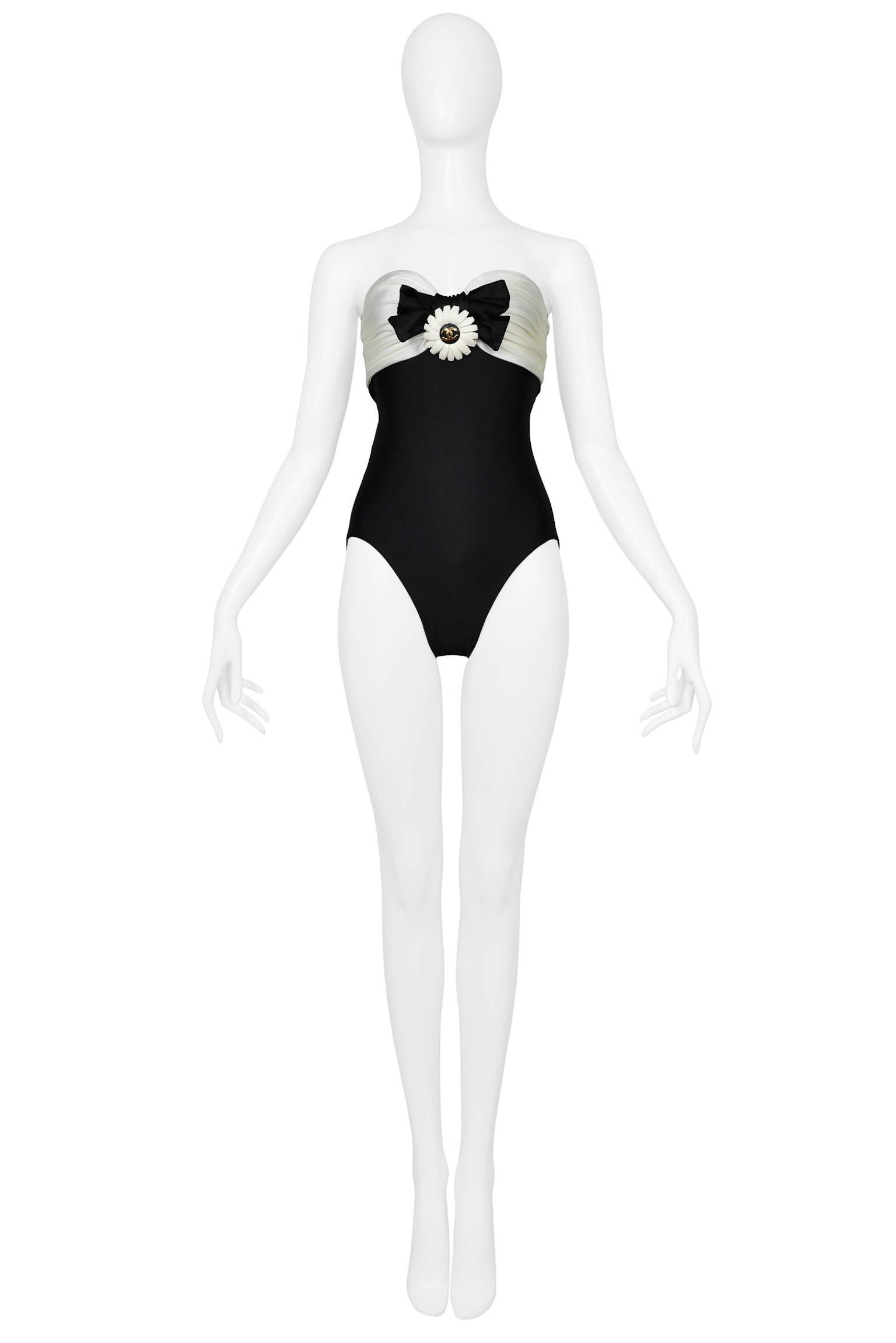 Vintage Chanel black and white swimsuit with black bow and cast or molded sculptural plastic off white daisy flower with gold CC emblem at front. This piece features an off-the-shoulder neckline, sweetheart bust line, and full cover bottom. Never