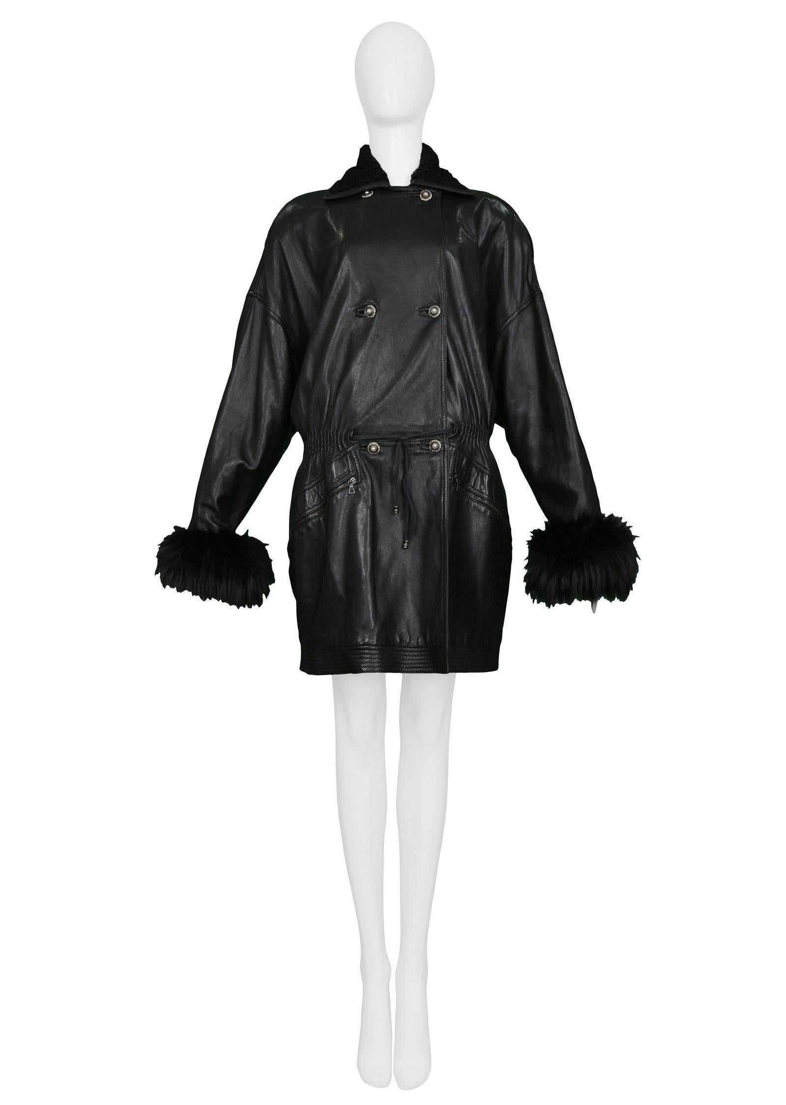 Vintage Gianni Versace black leather parka style coat with black fur cuffs and collar. The coat has a drawstring front waist, elastic back waist, soft shoulders, and decorative rhinestone buttons. Zipper pockets in front sides and quilted hem. Easy